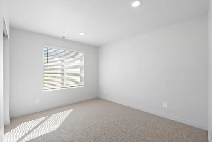 Carpeted room featuring a large window with blinds, recessed ceiling lighting, and light-toned walls