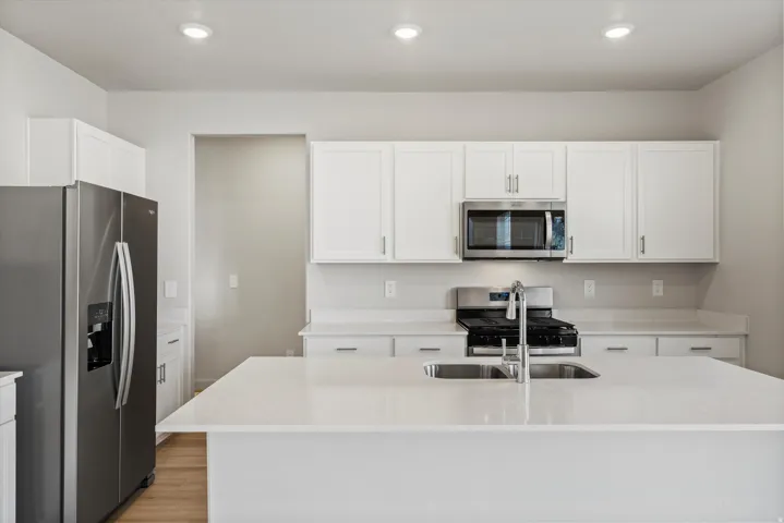 Kitchen featuring an island with a double basin sink, white cabinetry, stainless steel appliances, light countertops, and recessed lighting
