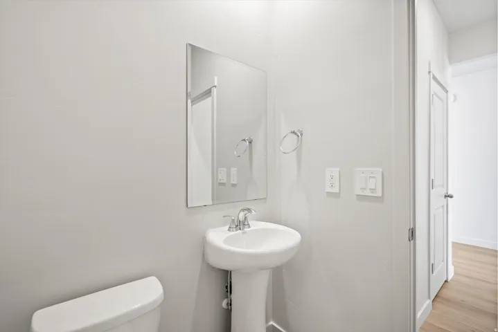 Bathroom featuring a pedestal sink, wall-mounted mirror, and a toilet