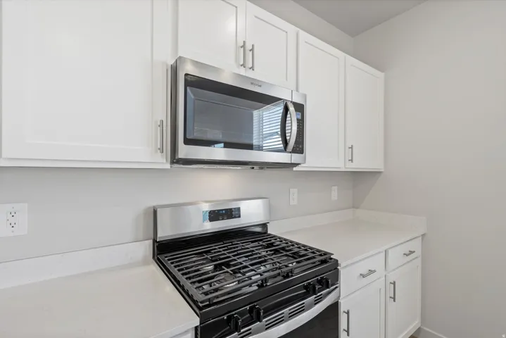 Kitchen featuring white shaker cabinetry, stainless steel microwave, stainless steel gas range, light-toned countertops, and light gray wall paint