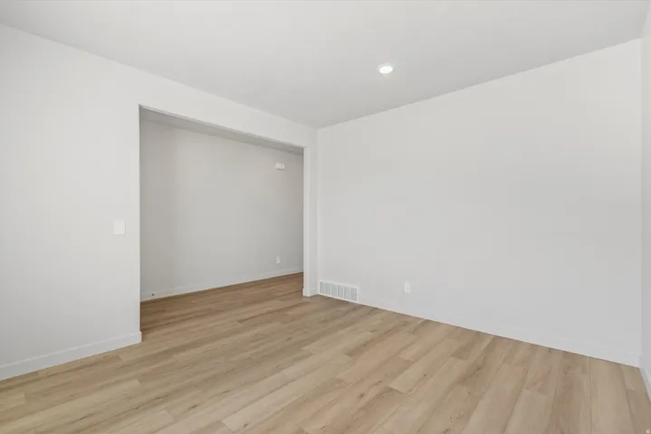 Spacious room with light wood-finish flooring, recessed lighting, white baseboards, and a wide entryway