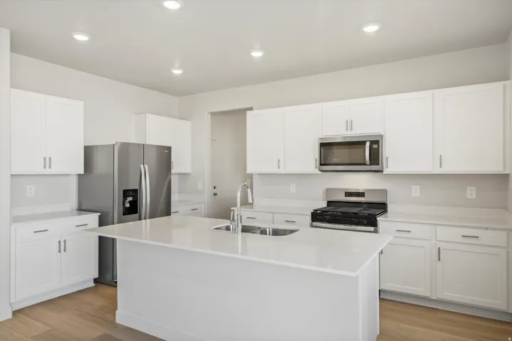 Modern kitchen featuring a central island with an undermount sink, white shaker cabinetry, stainless steel appliances, and light wood-finish flooring