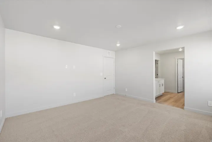 Spacious room featuring neutral carpet flooring, recessed lighting, and a white interior door