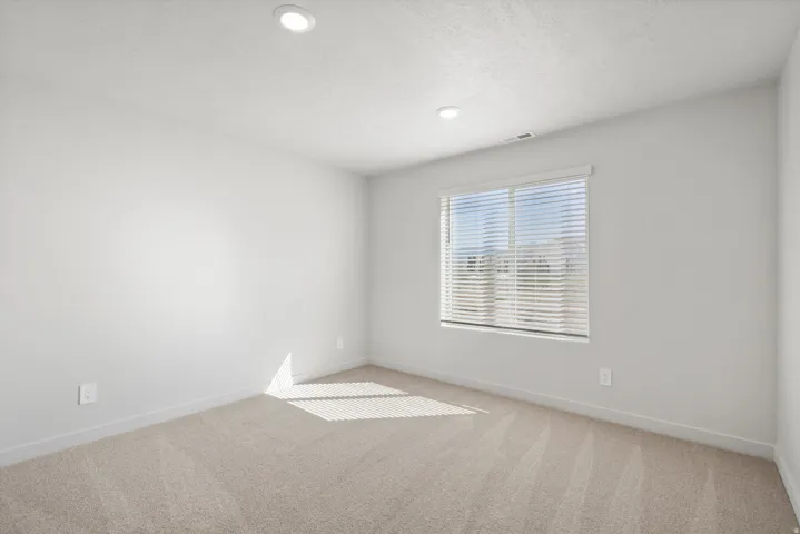 Spacious room featuring neutral carpeting, a large window with horizontal blinds, recessed ceiling lighting, and light-toned wall paint