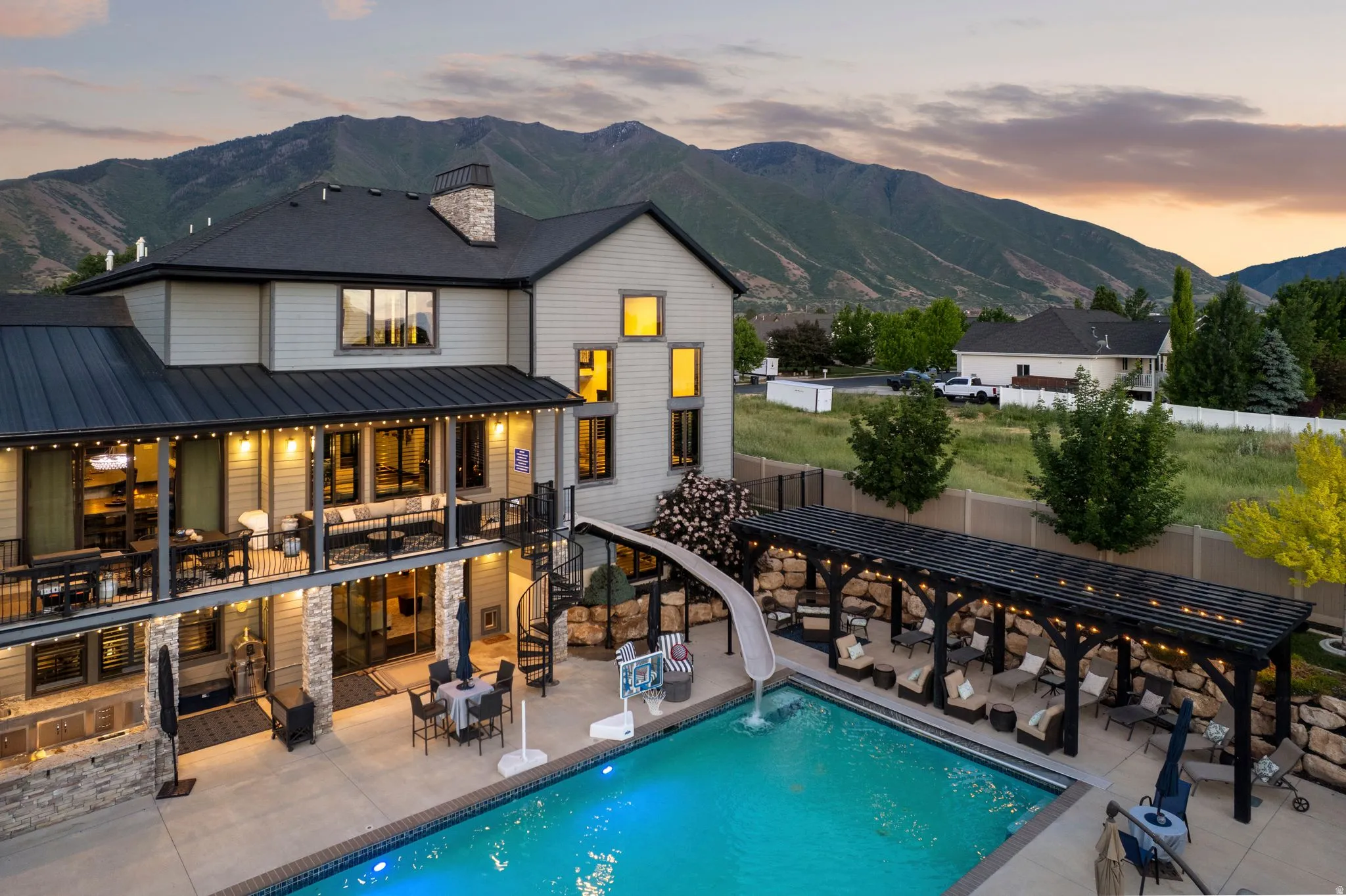 Expansive backyard featuring a large swimming pool with a slide, a multi-level patio with stone pillars, a built-in outdoor kitchen, and a covered lounge area with a pergola