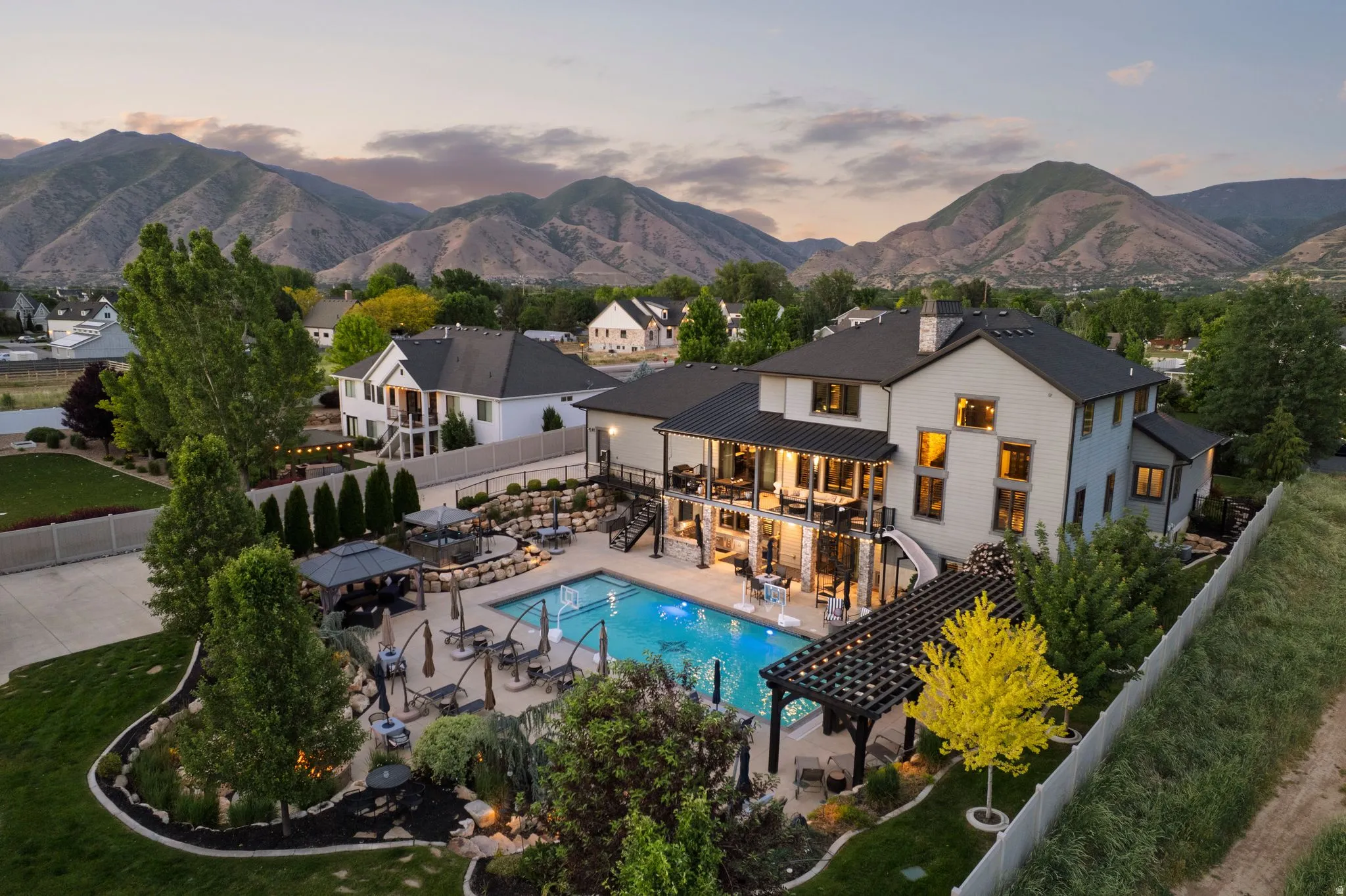 Expansive backyard featuring a large swimming pool, multiple patio areas with umbrellas, and a shaded pergola