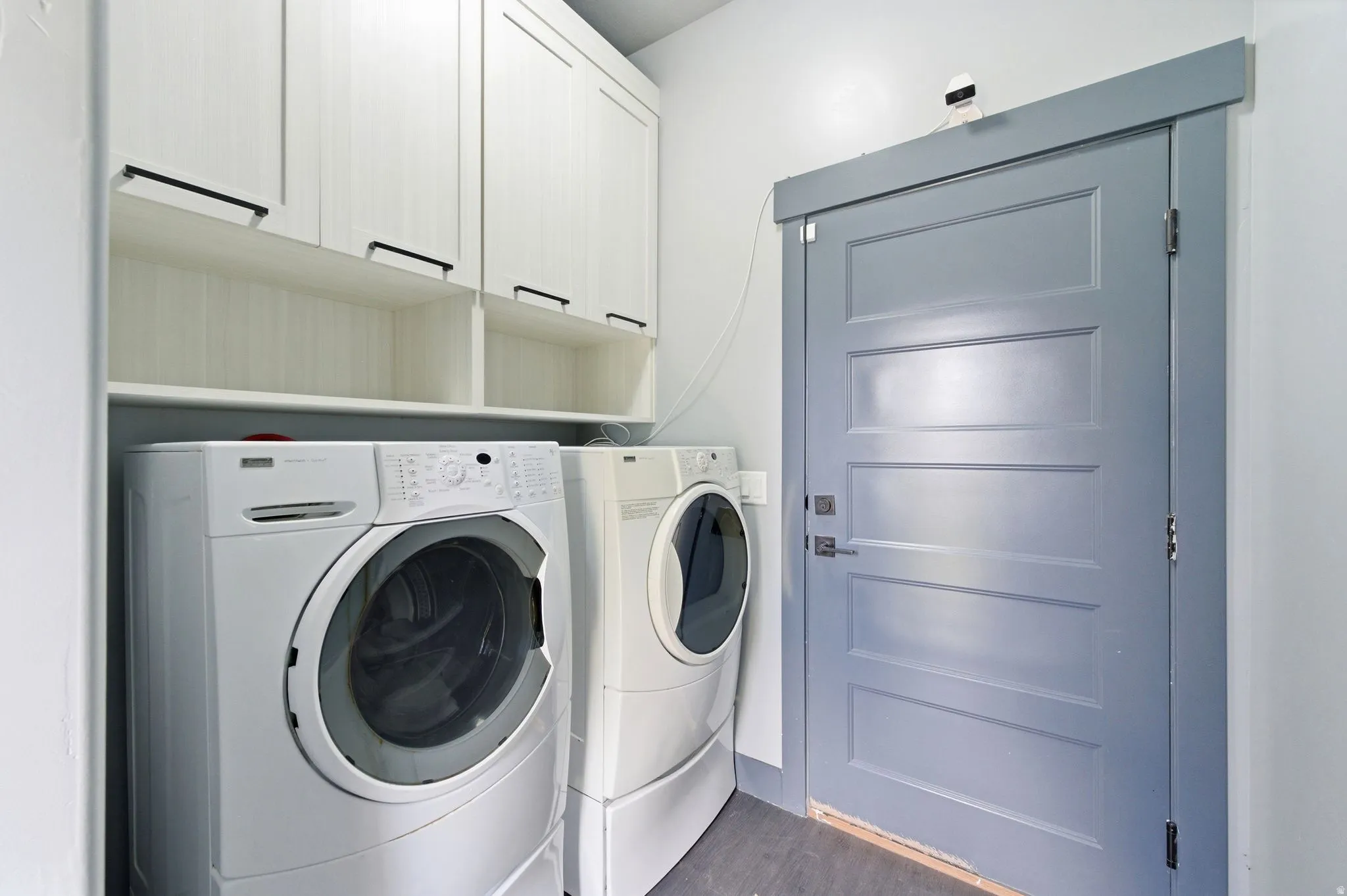 Dedicated laundry area featuring white upper cabinetry with dark hardware and open shelving