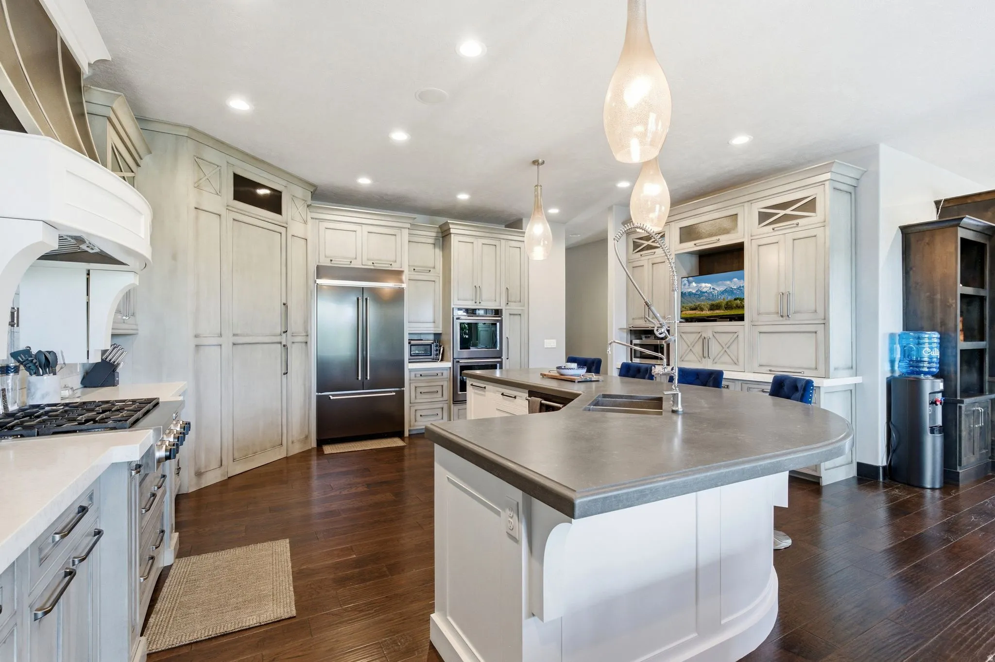 Spacious kitchen featuring an expansive center island, integrated stainless steel appliances, abundant cabinetry, wood-finish flooring, and recessed lighting