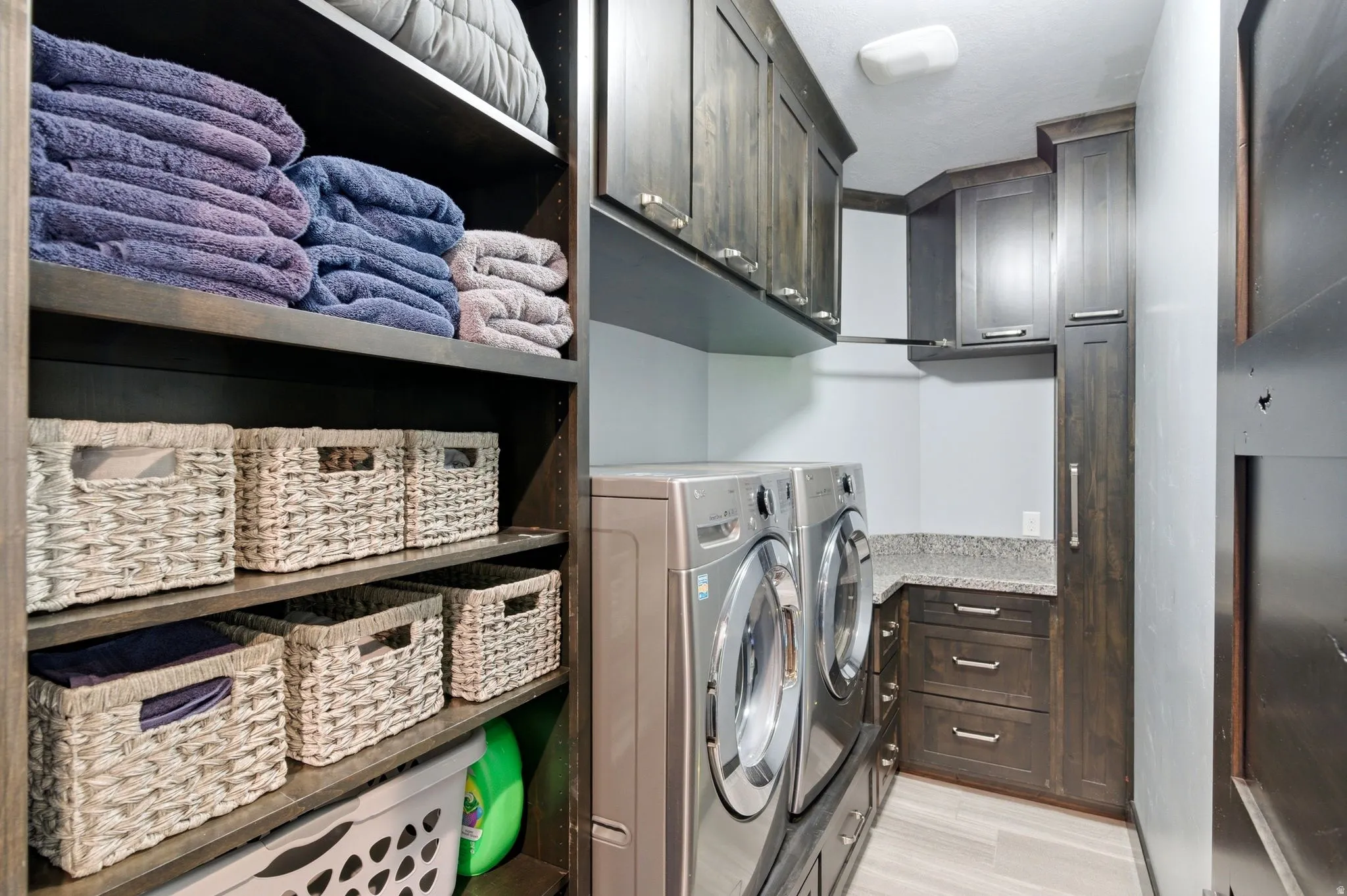 Dedicated laundry room featuring wood-finish cabinetry, granite-style countertops, built-in shelving, and light wood-finish flooring