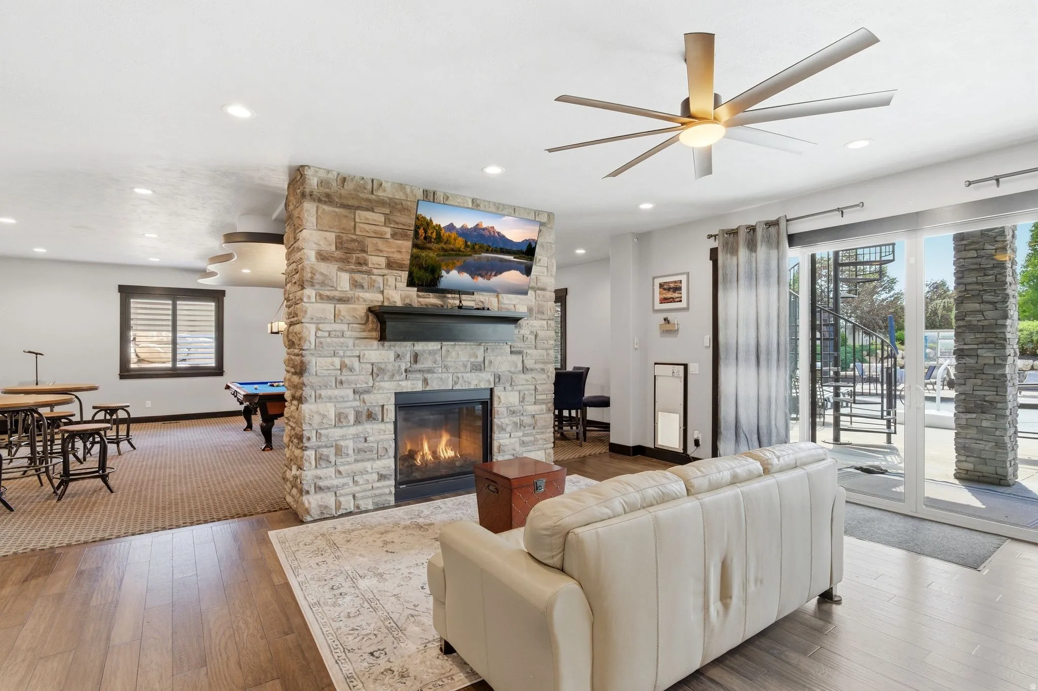 Stone-clad fireplace feature wall with integrated mantel, recessed lighting, wood-finish flooring, and a multi-blade ceiling fan