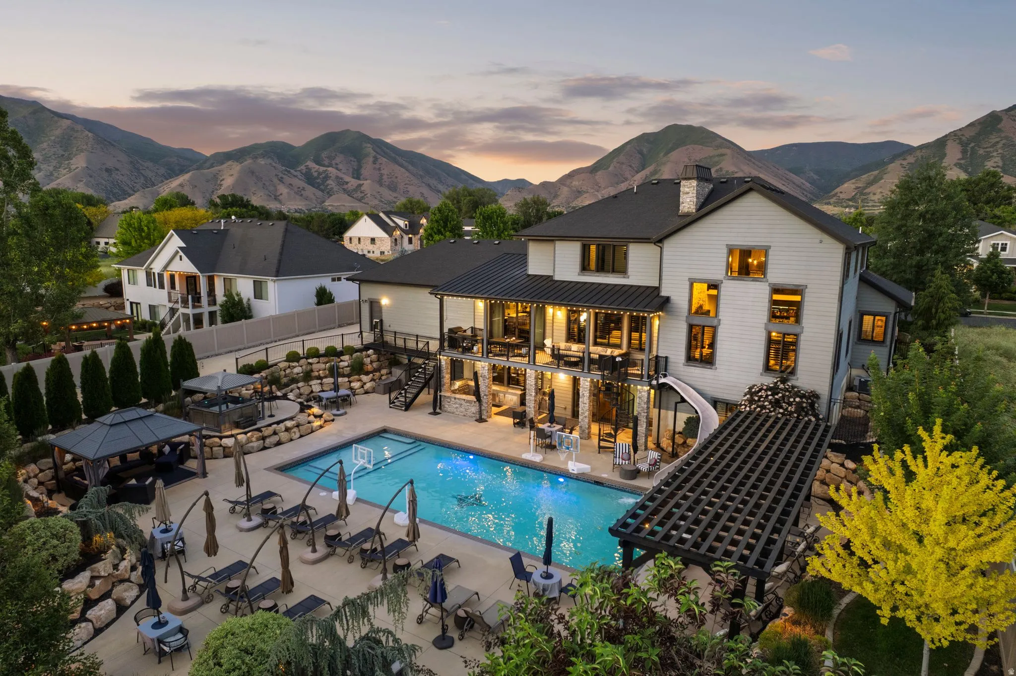 Expansive rear exterior featuring a swimming pool, multiple outdoor seating areas, and a tiered rock wall landscape
