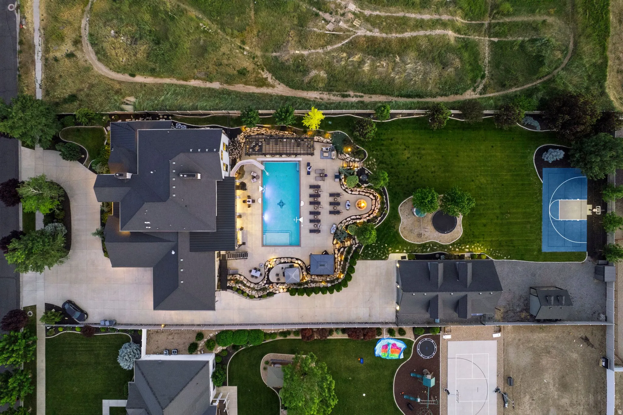 Expansive property featuring a meticulously landscaped backyard with a swimming pool, multiple patio areas, and a full basketball court