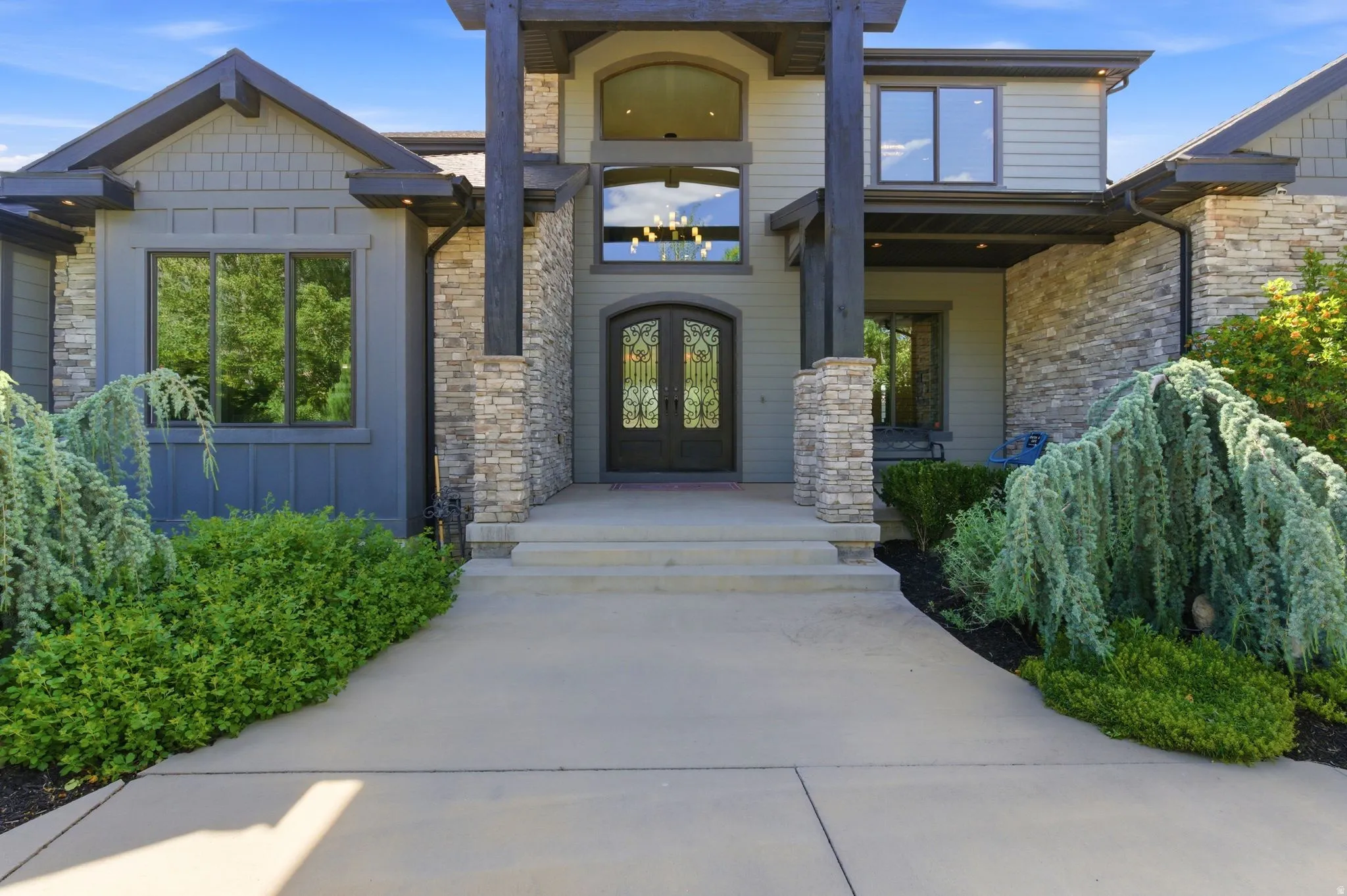 Grand entryway featuring a double door with decorative glass, flanked by stone veneer columns and wood beam accents