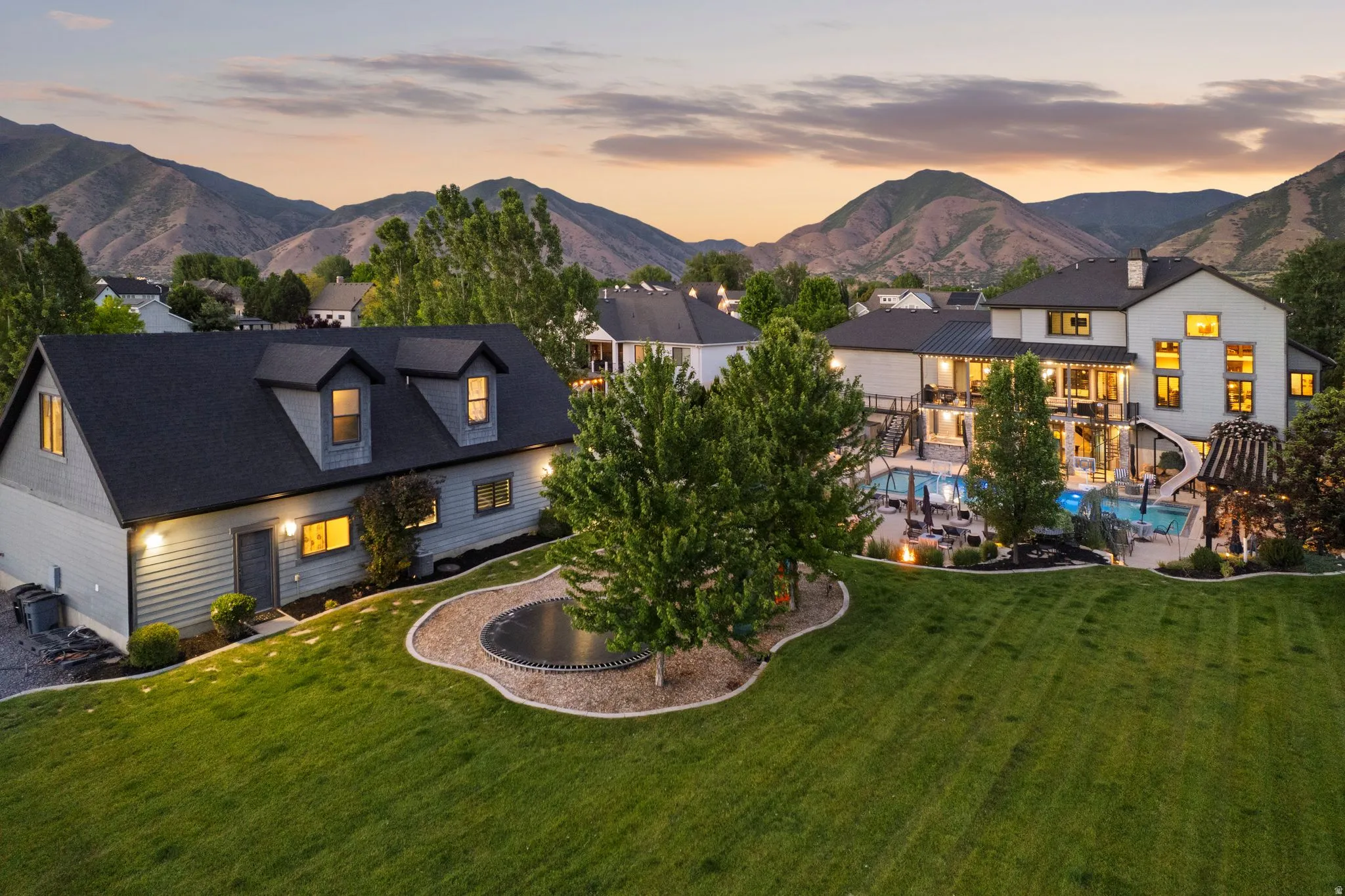 Expansive property featuring a large manicured lawn, a swimming pool with an integrated slide, a separate pool area, and an additional auxiliary structure with dormer windows