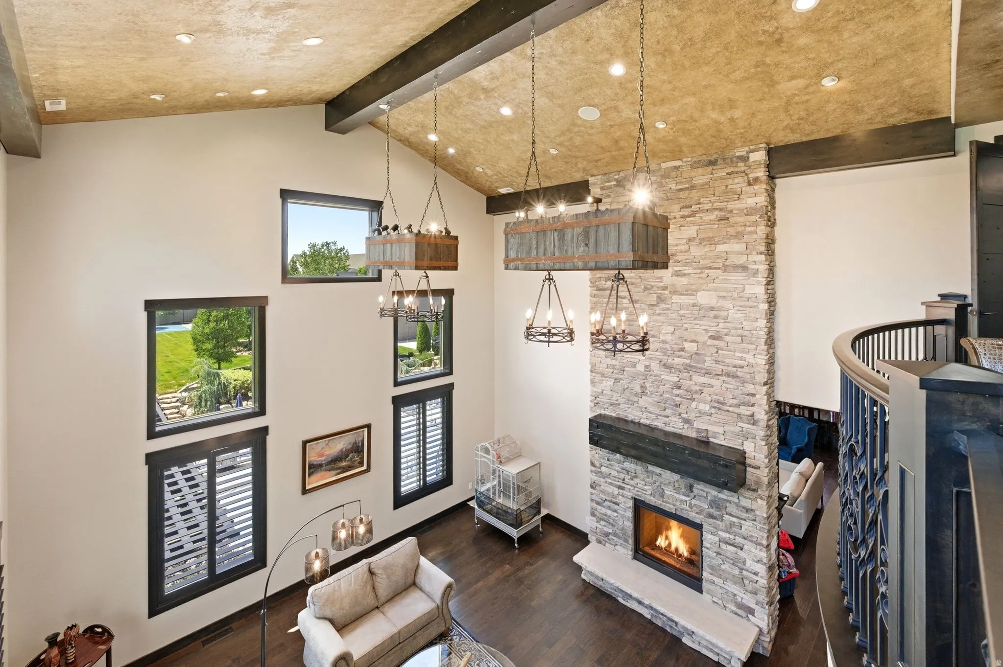 Two-story living area with a stone fireplace, wood-finish flooring, and multiple windows