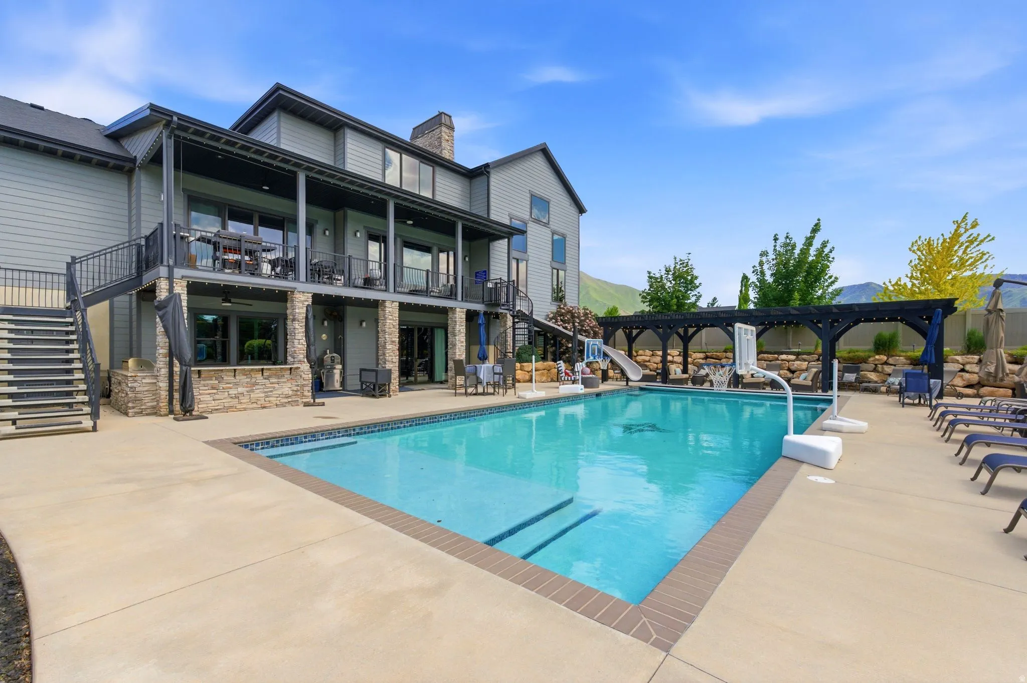 Expansive outdoor area featuring a swimming pool with integrated steps, a surrounding concrete patio, and an open pergola structure