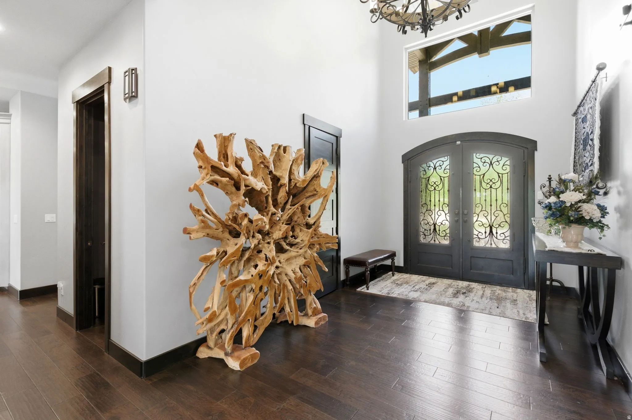 Grand entry featuring dark double doors with decorative wrought iron glass inserts, a high transom window, and dark wood-finish flooring