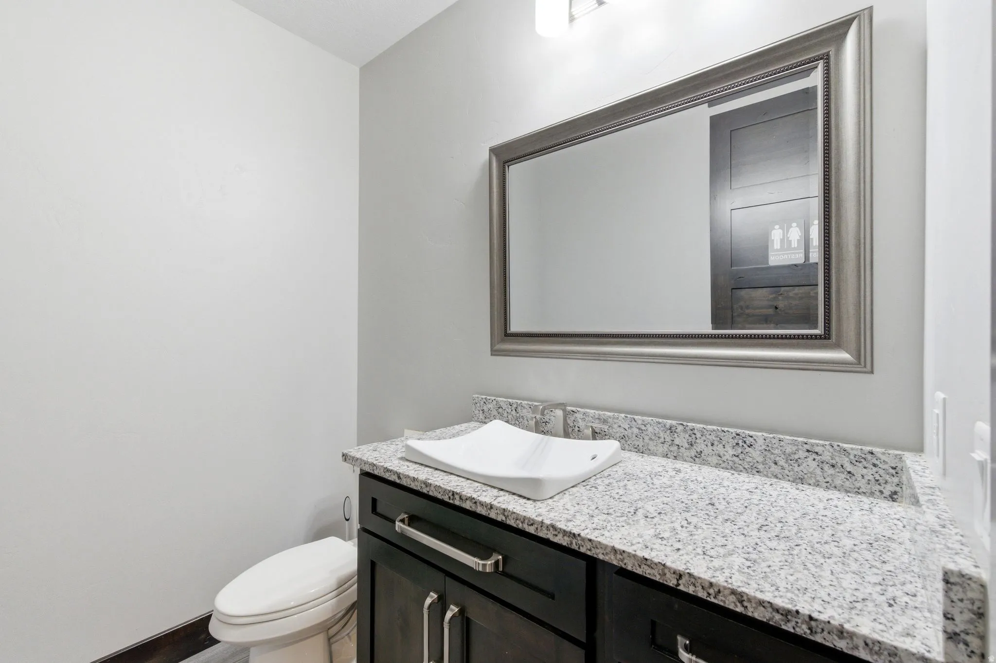 Powder room featuring a dark wood-finish vanity with chrome hardware, a light-colored granite countertop, and a contemporary vessel sink