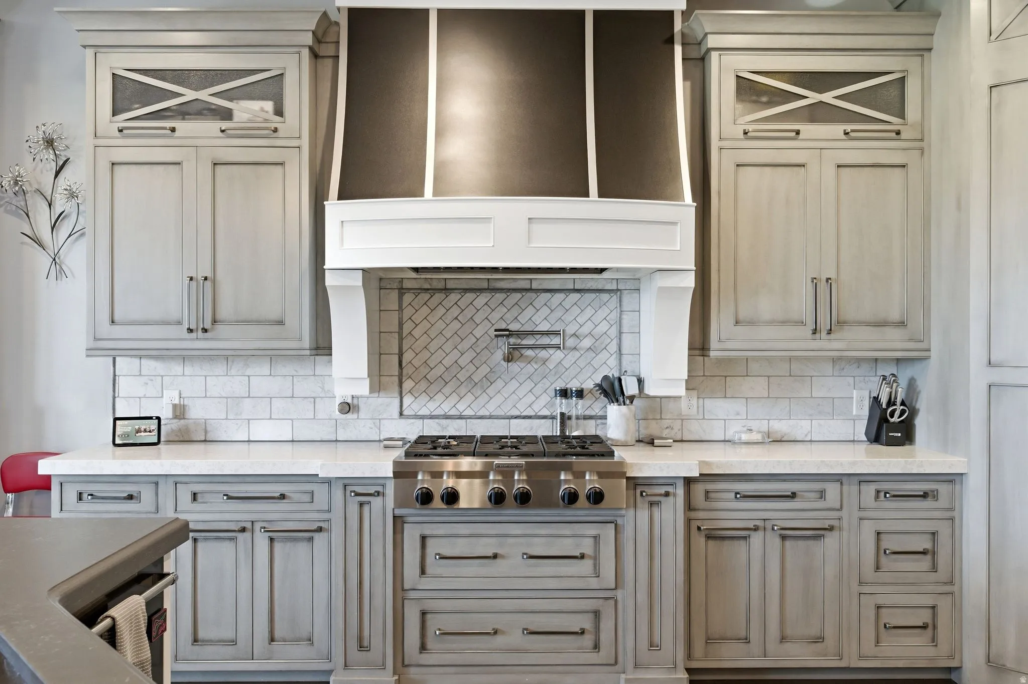 Gourmet kitchen featuring a stainless steel gas range, custom range hood, subway tile backsplash with a herringbone pattern above the range, light-toned cabinetry, and solid surface countertops