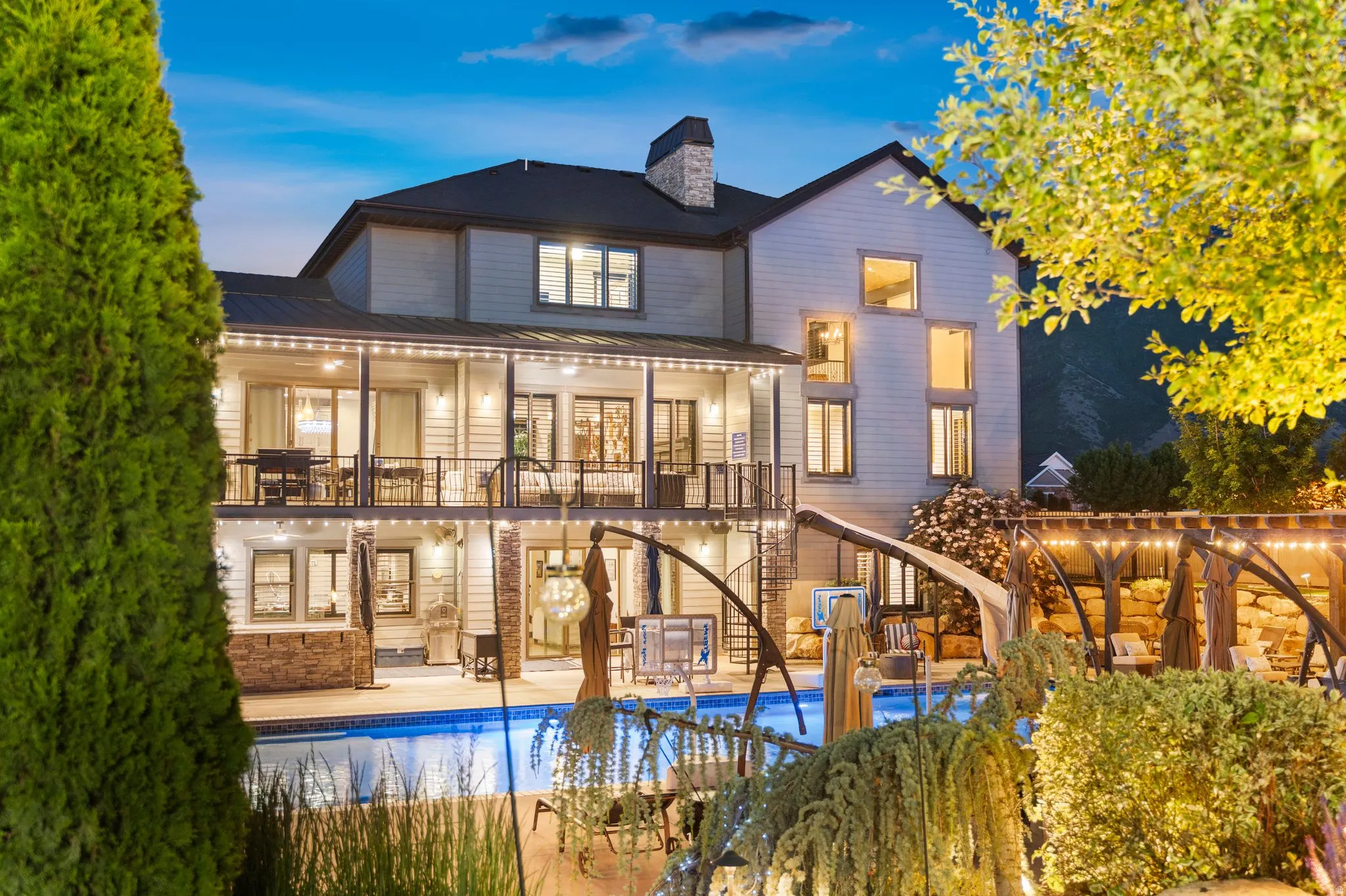Multi-story residence featuring a large swimming pool, expansive outdoor entertaining areas, a stone chimney, and multiple balconies with dark metal railings