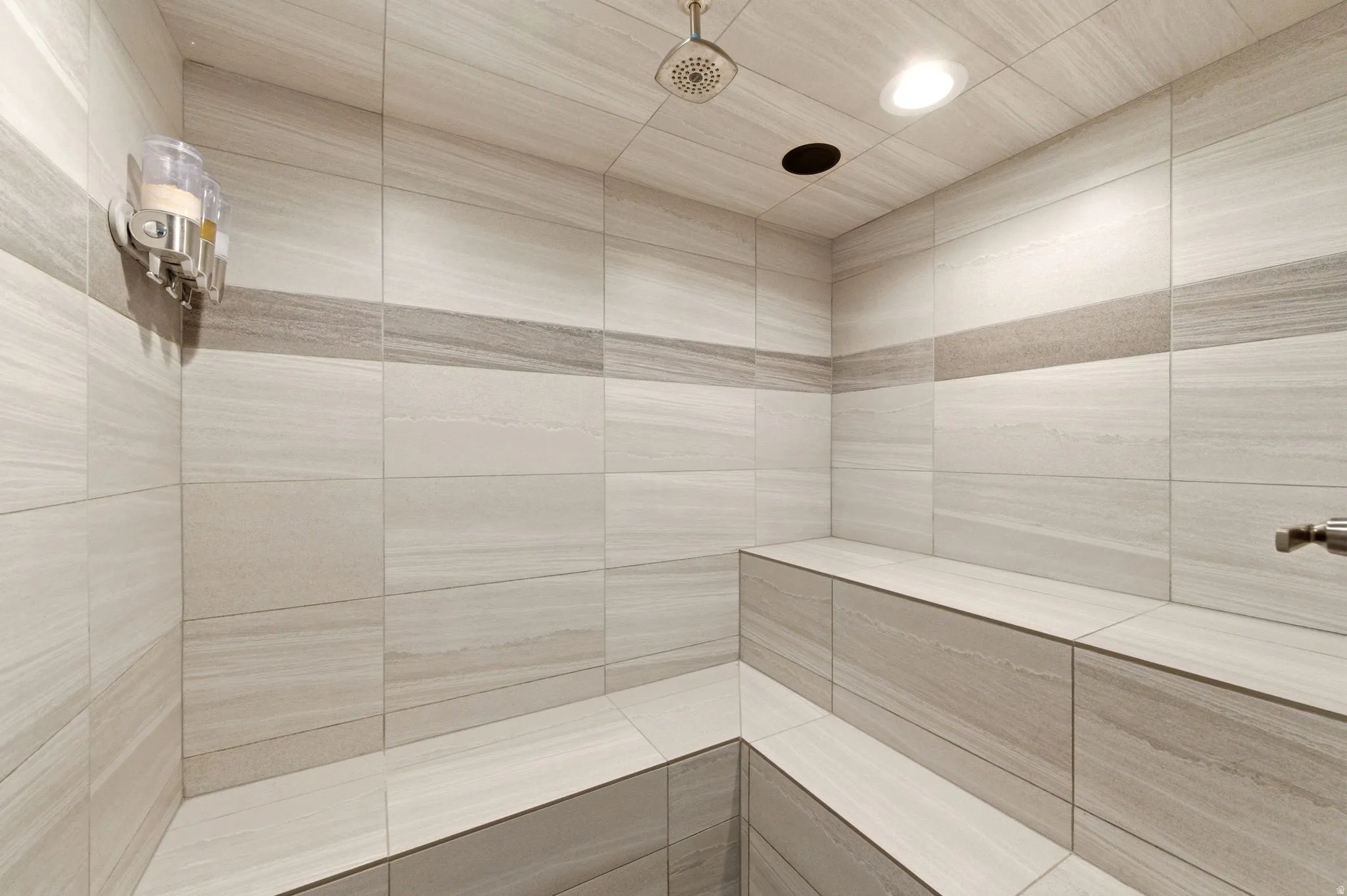Tiled shower space featuring integrated bench seating, a rain shower head, and recessed lighting