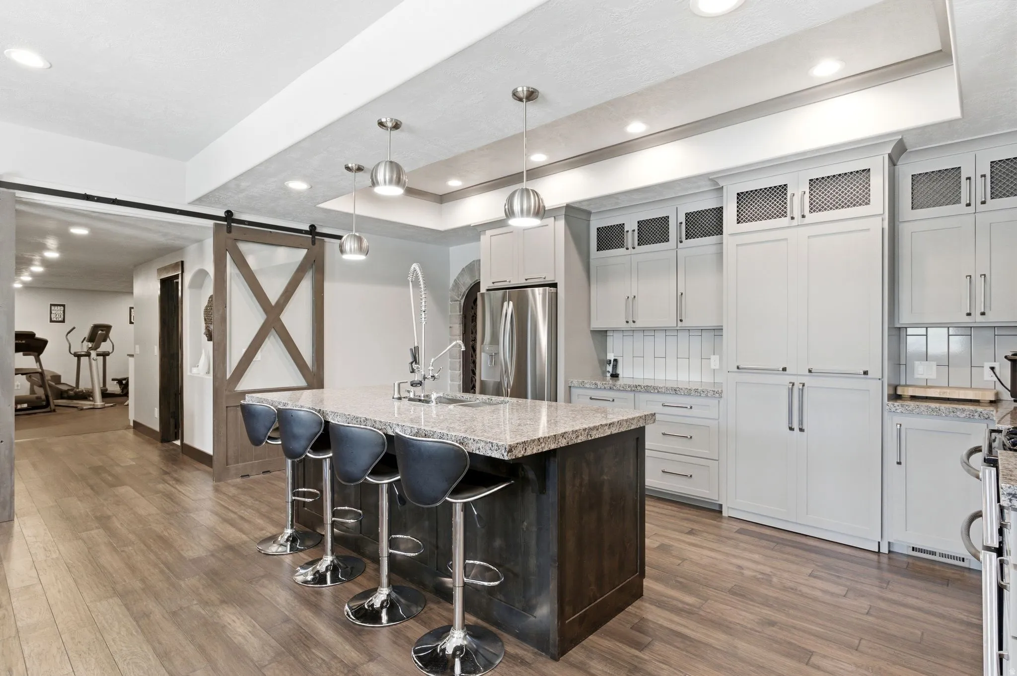 Kitchen featuring a stone-look countertop island with sink, stainless steel appliances, light-toned cabinetry, and wood-finish flooring