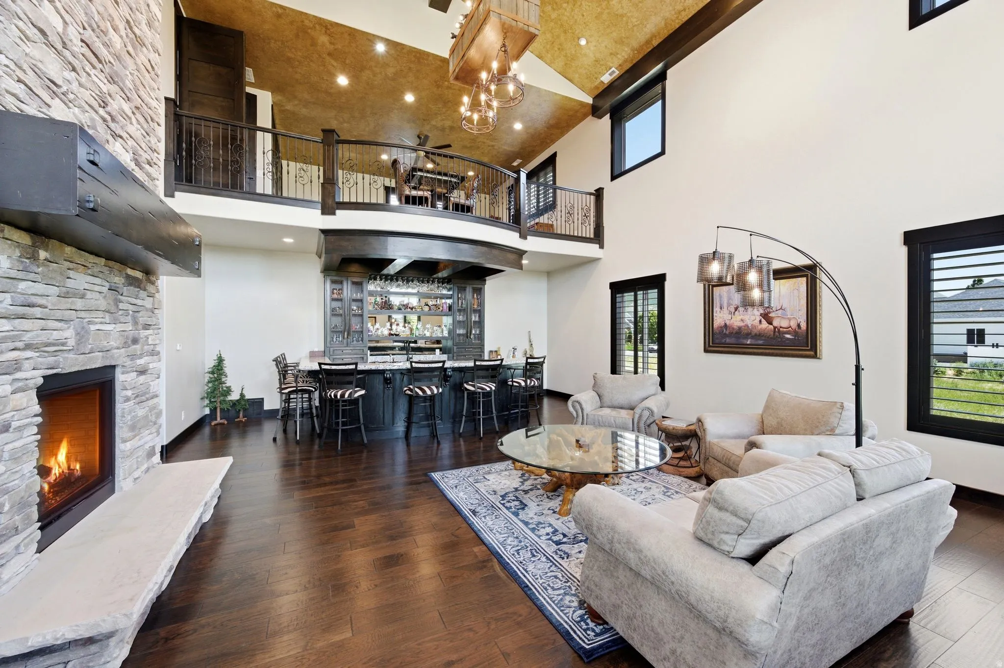 Two-story living area featuring a stone fireplace with a stone hearth, an integrated wet bar, wood-finish flooring, and a second-story balcony overlooking the space
