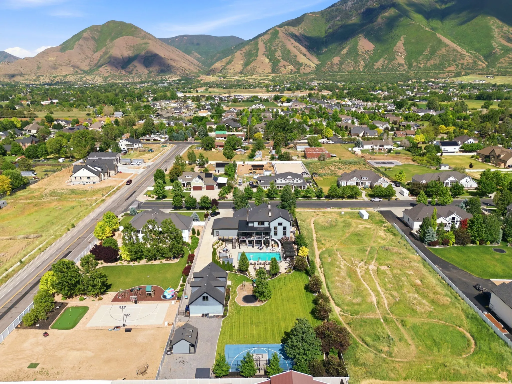 Expansive mountain backdrop framing a property featuring a pool, basketball court, and green lawn areas