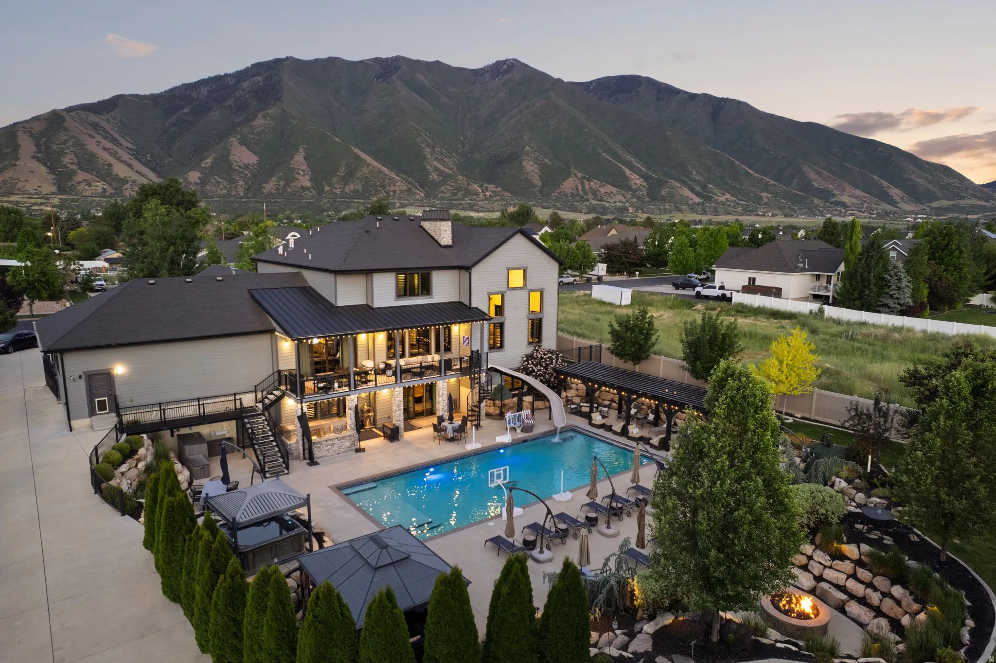 Expansive backyard with a rectangular swimming pool, multiple pergolas, and a tiered rock garden with fire pit