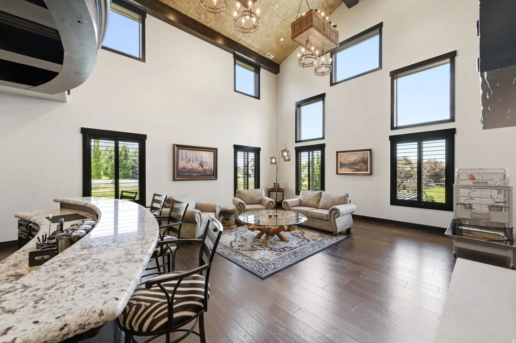 Great room featuring soaring ceilings with exposed wood beams, hardwood flooring, and multiple windows with dark trim
