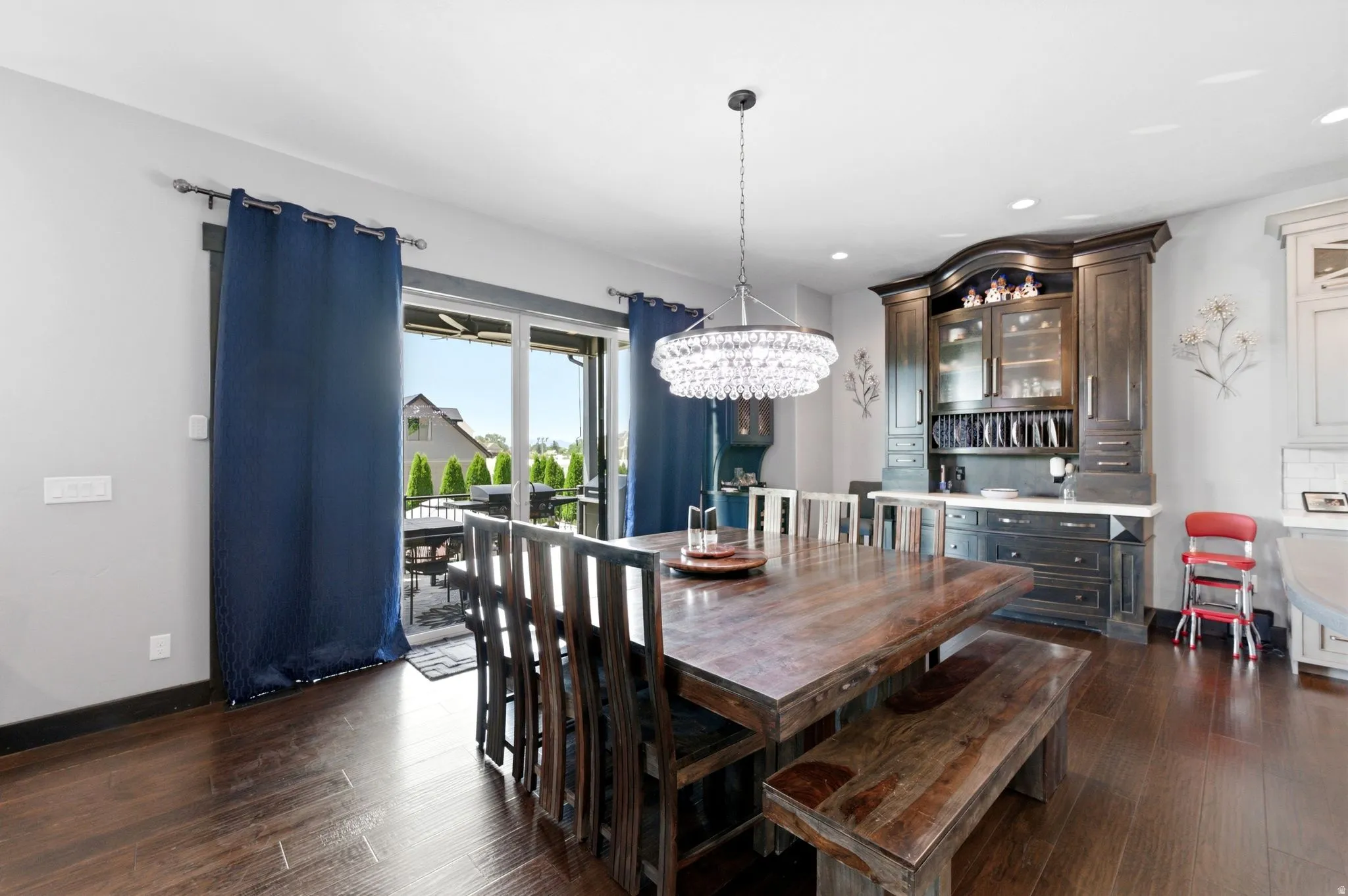 Spacious dining area featuring wood-finish flooring, a built-in dark wood hutch with glass-front cabinetry, an ornate chandelier, and a sliding glass door opening to an outdoor patio