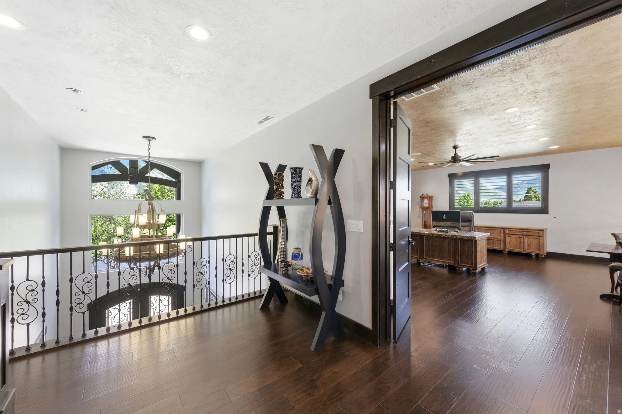 Upper-level landing featuring dark wood-finish flooring, a wrought iron railing, and recessed lighting