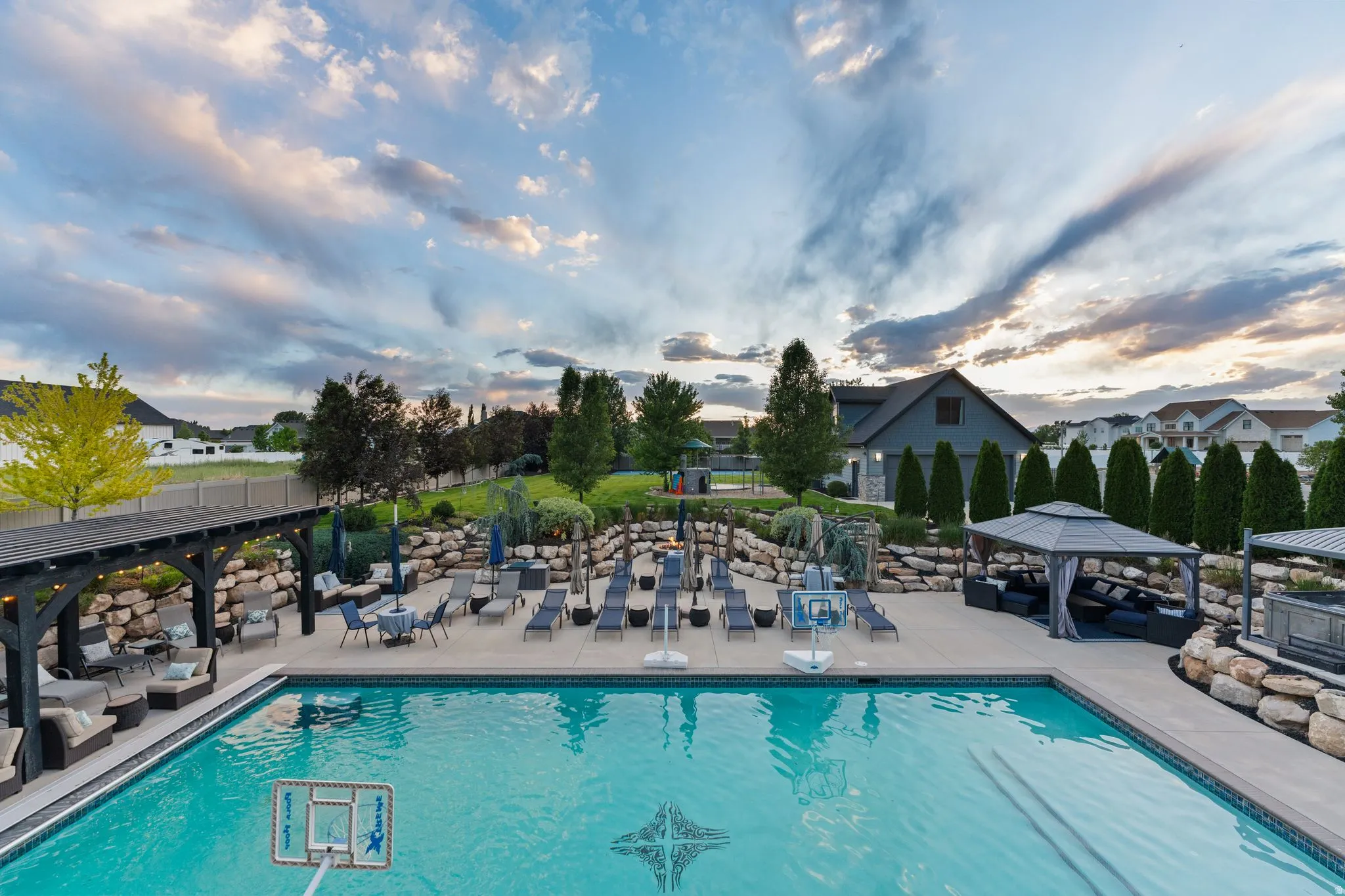 Expansive outdoor living area featuring a large swimming pool with decorative tile inlay, a pergola-covered patio, and a separate gazebo