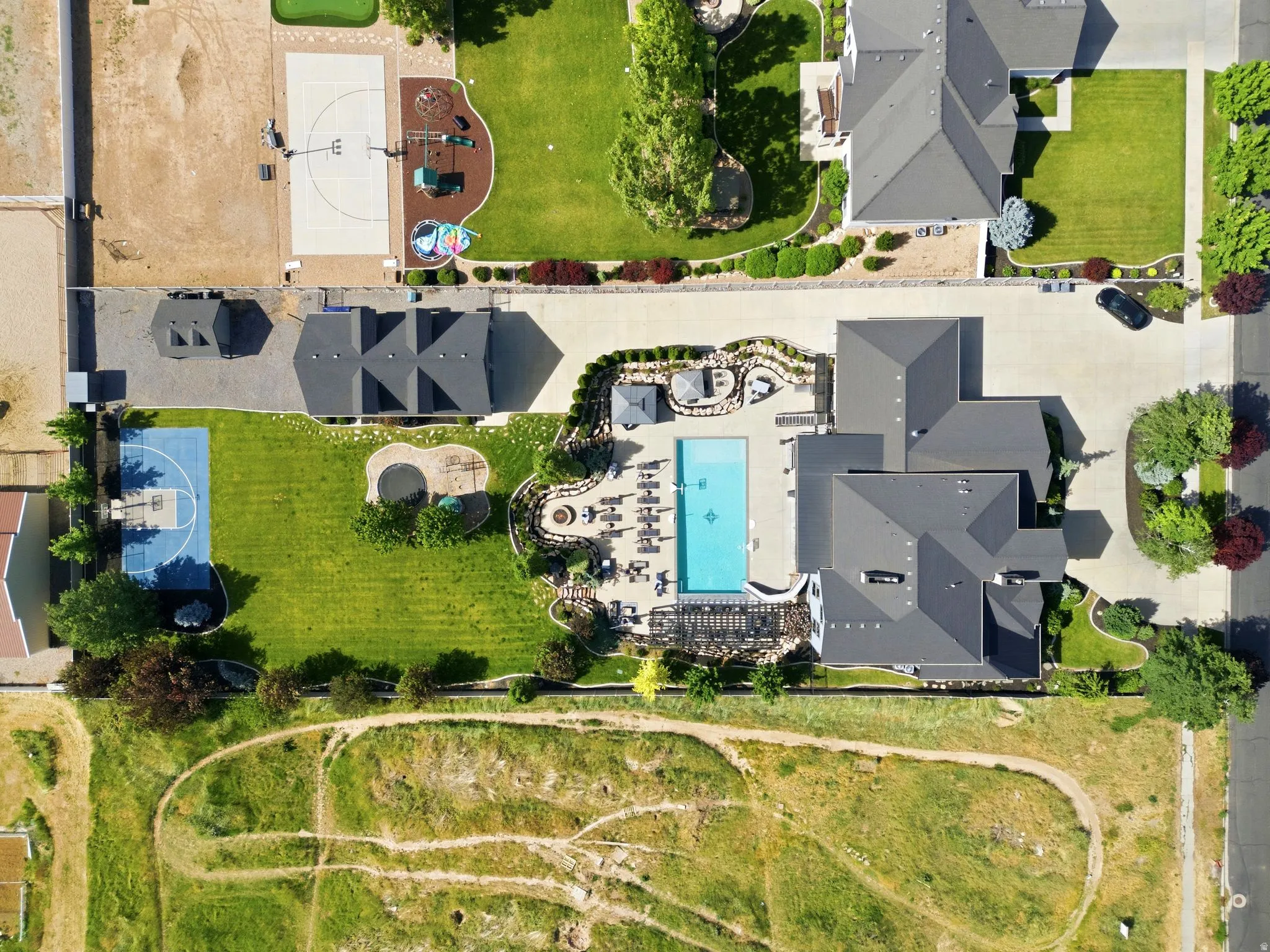 Expansive property featuring a large in-ground swimming pool surrounded by a paved patio, a full basketball court, and mature landscaping