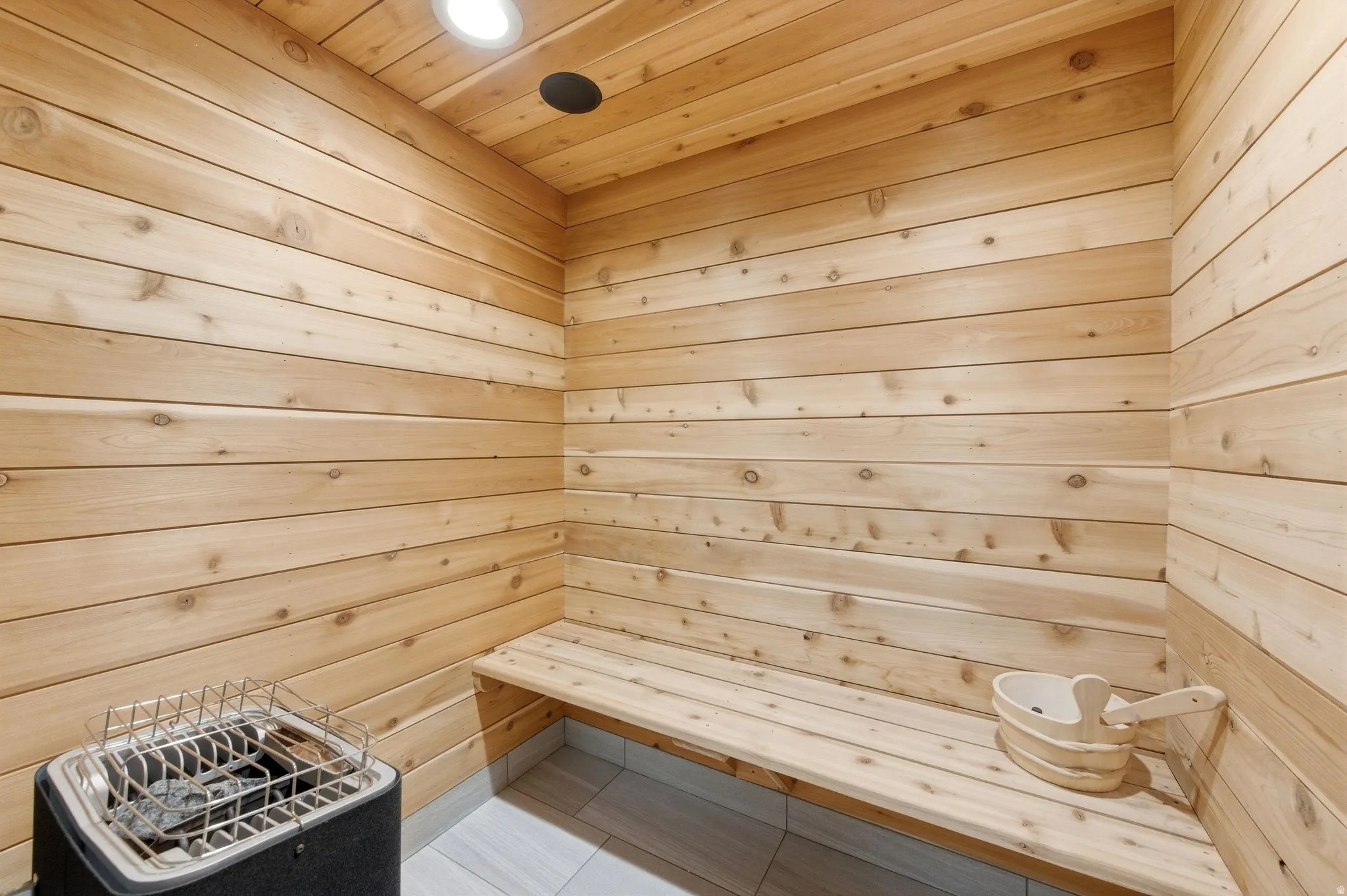 Interior sauna featuring light wood paneling, a built-in wood bench, recessed lighting, and a floor-mounted heater