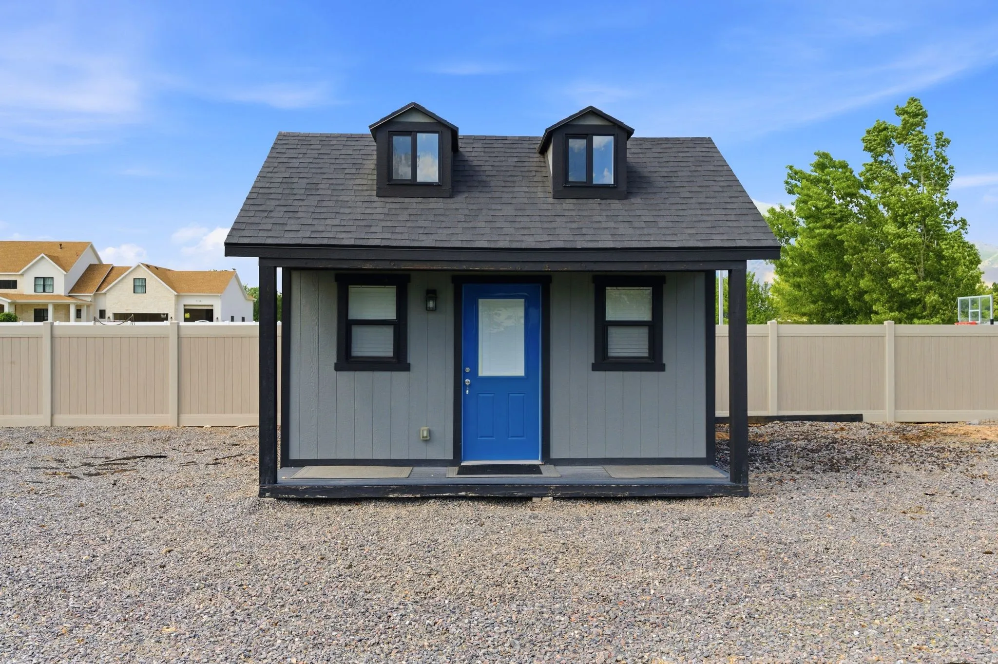 Compact outbuilding featuring vertical siding, a dark asphalt shingle roof, and two dormer windows