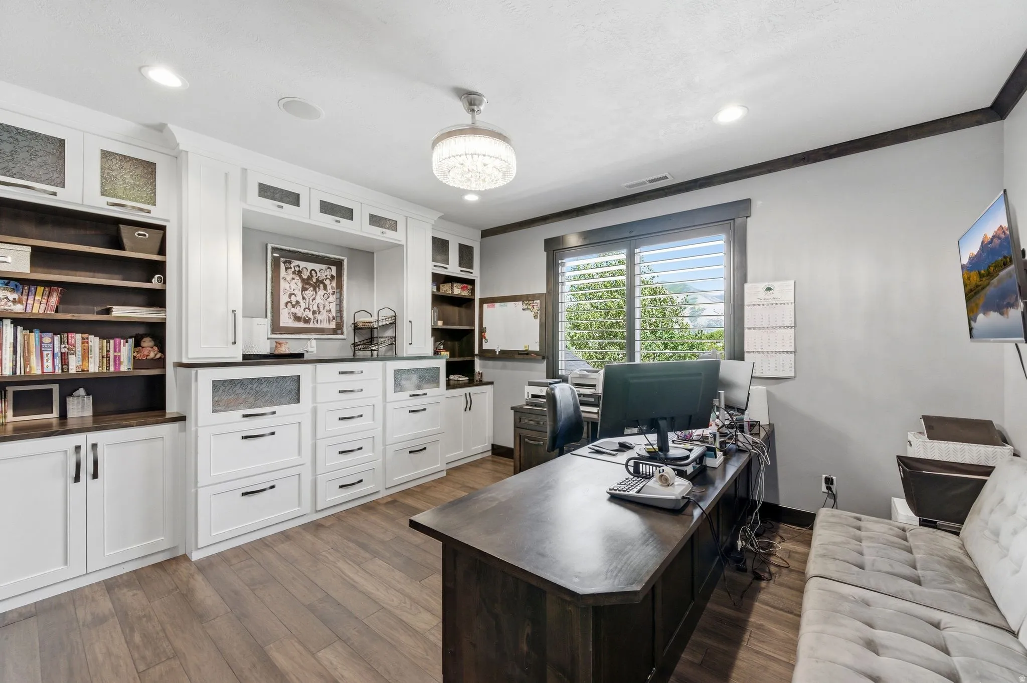 Office space featuring extensive built-in white cabinetry and shelving, dark wood-finish flooring, a contemporary chandelier, recessed lighting, and a window with horizontal blinds