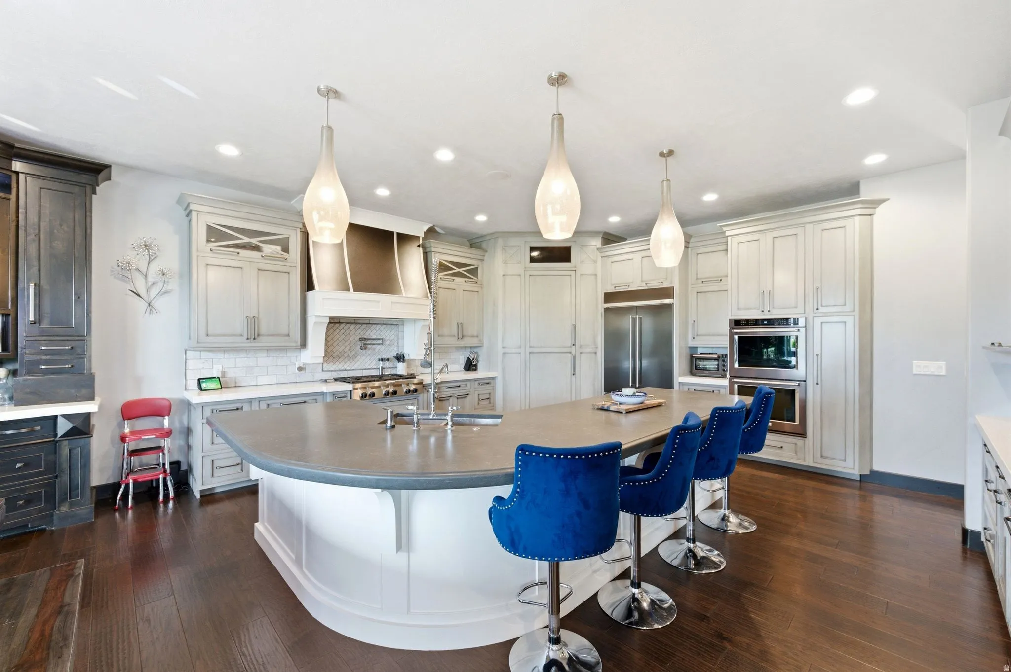 Gourmet kitchen featuring a large central island, white shaker-style cabinetry, dark wood-finish flooring, stainless steel appliances, and a tiled backsplash