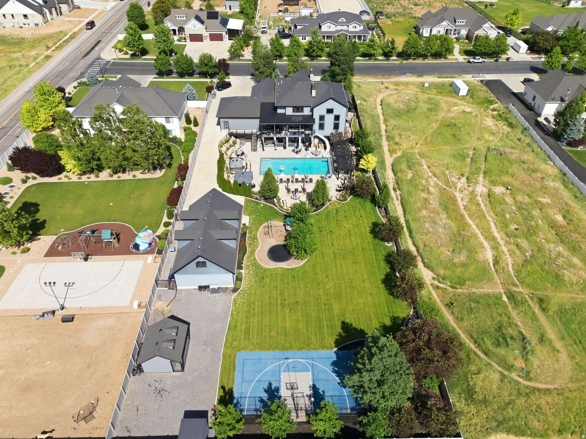 Expansive property featuring a large in-ground swimming pool, a dedicated sports court, a meticulously maintained lawn, and mature landscaping