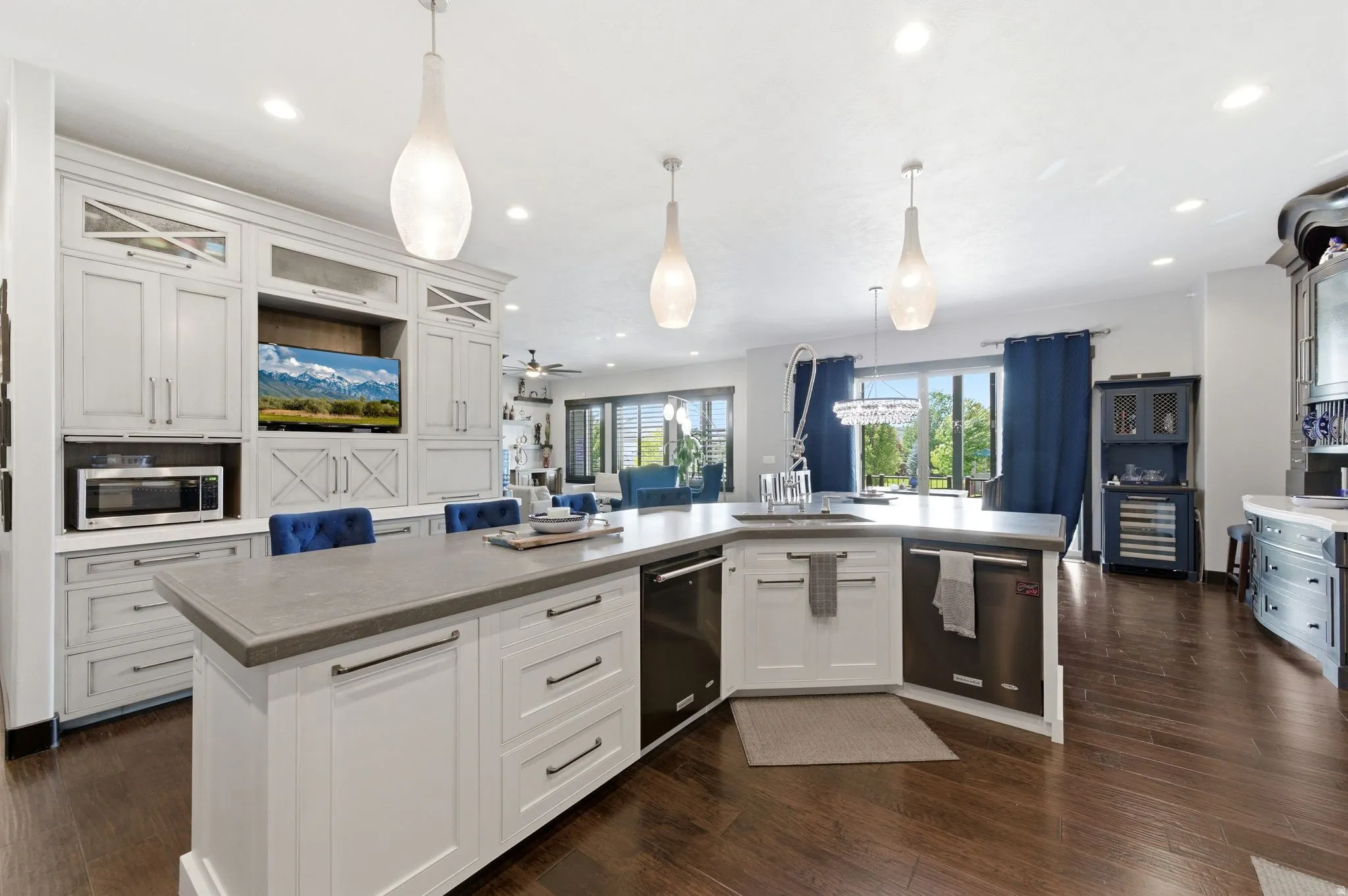 Gourmet kitchen featuring a large L-shaped island with a built-in sink and stainless steel appliances, white cabinetry with dark pulls, wood-finish flooring, and recessed and pendant lighting