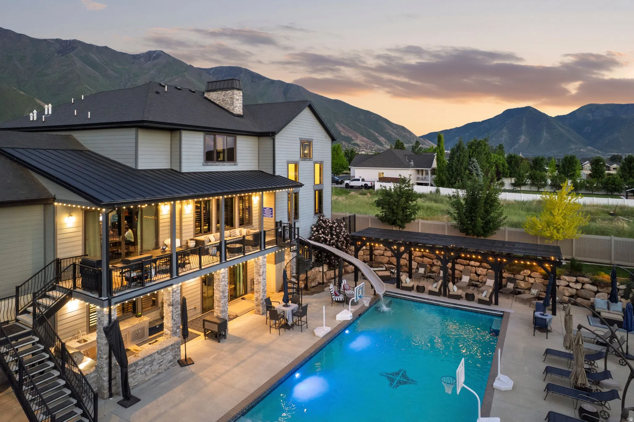 Expansive exterior featuring a large swimming pool with an integrated slide, a covered outdoor kitchen, and a covered patio