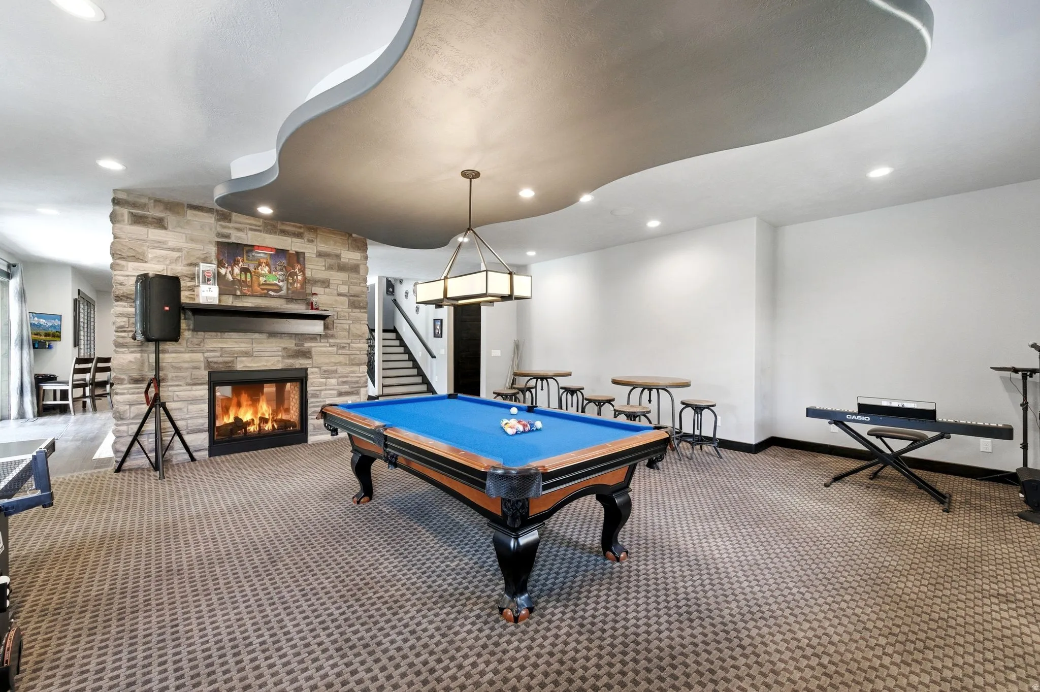 Recreation room featuring a stone-clad fireplace, patterned carpeting, recessed lighting, and a multi-level ceiling design