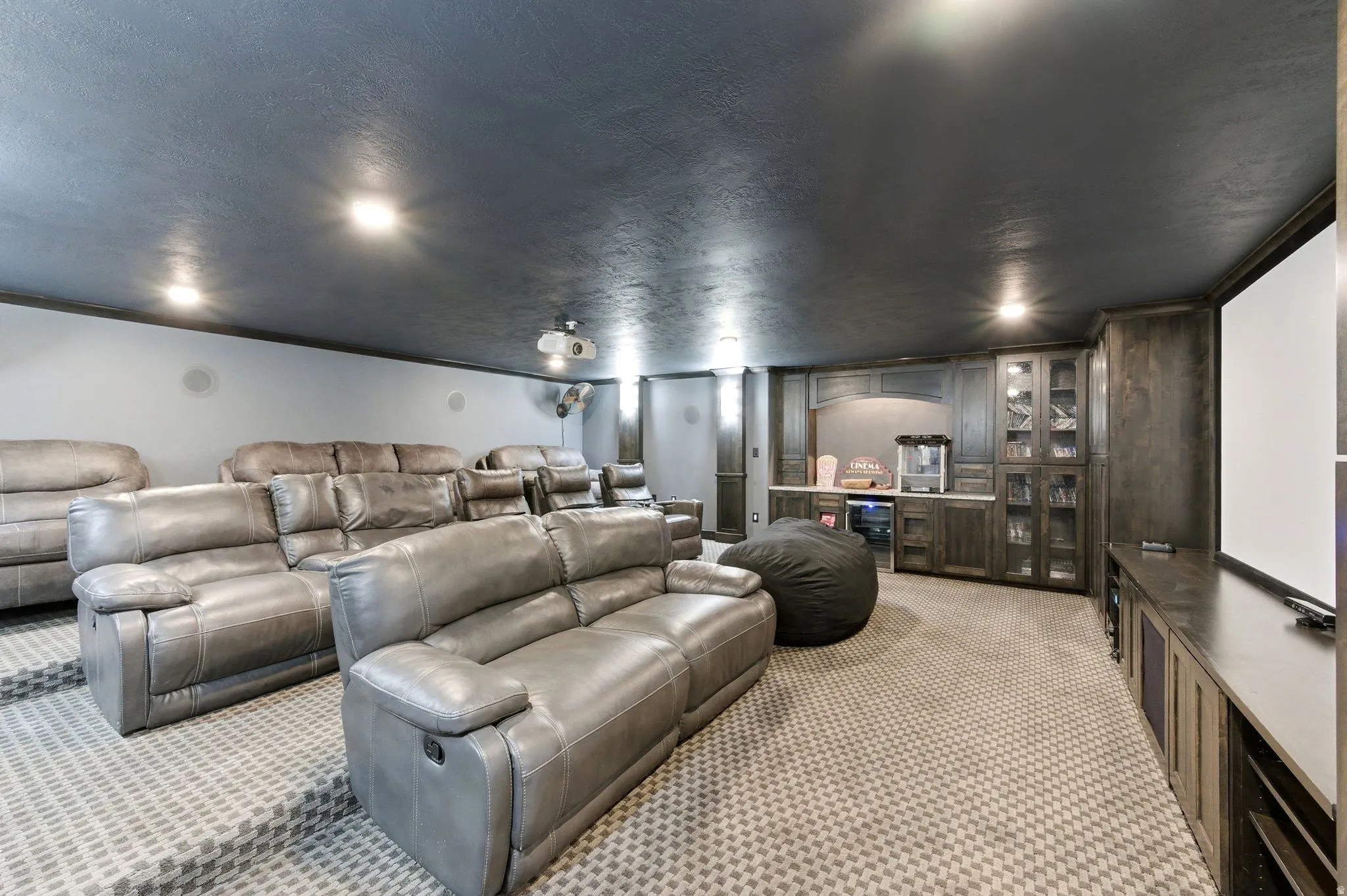 Dedicated media room featuring tiered seating, built-in entertainment cabinetry, a large projection screen, a wet bar with built-in appliances, and recessed lighting