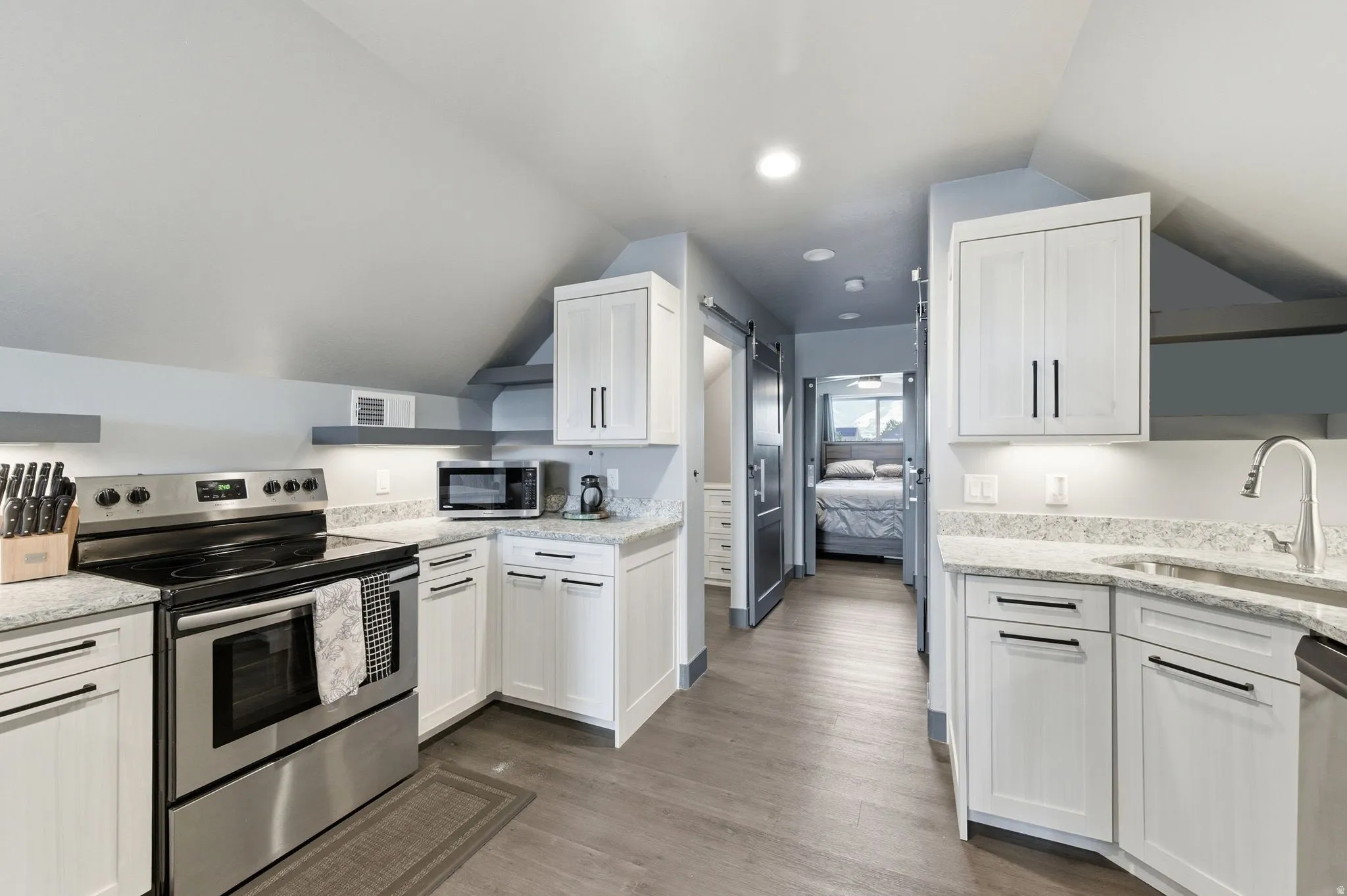 Contemporary kitchen featuring stainless steel appliances, white cabinetry, light granite countertops, recessed lighting, and wood-finish flooring