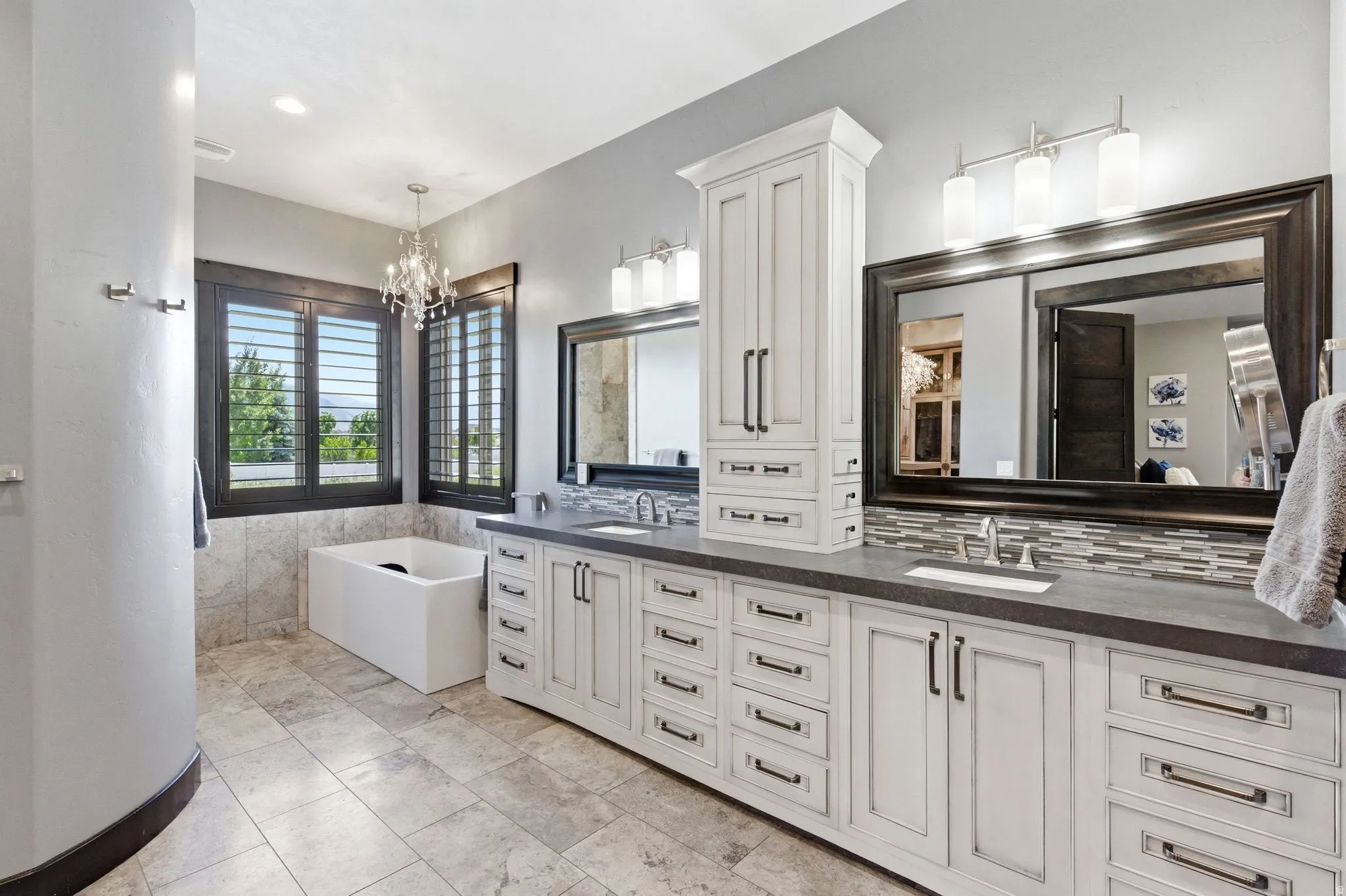 Bathroom featuring a freestanding soaking tub, wood-finish plantation shutters, and a chandelier light fixture