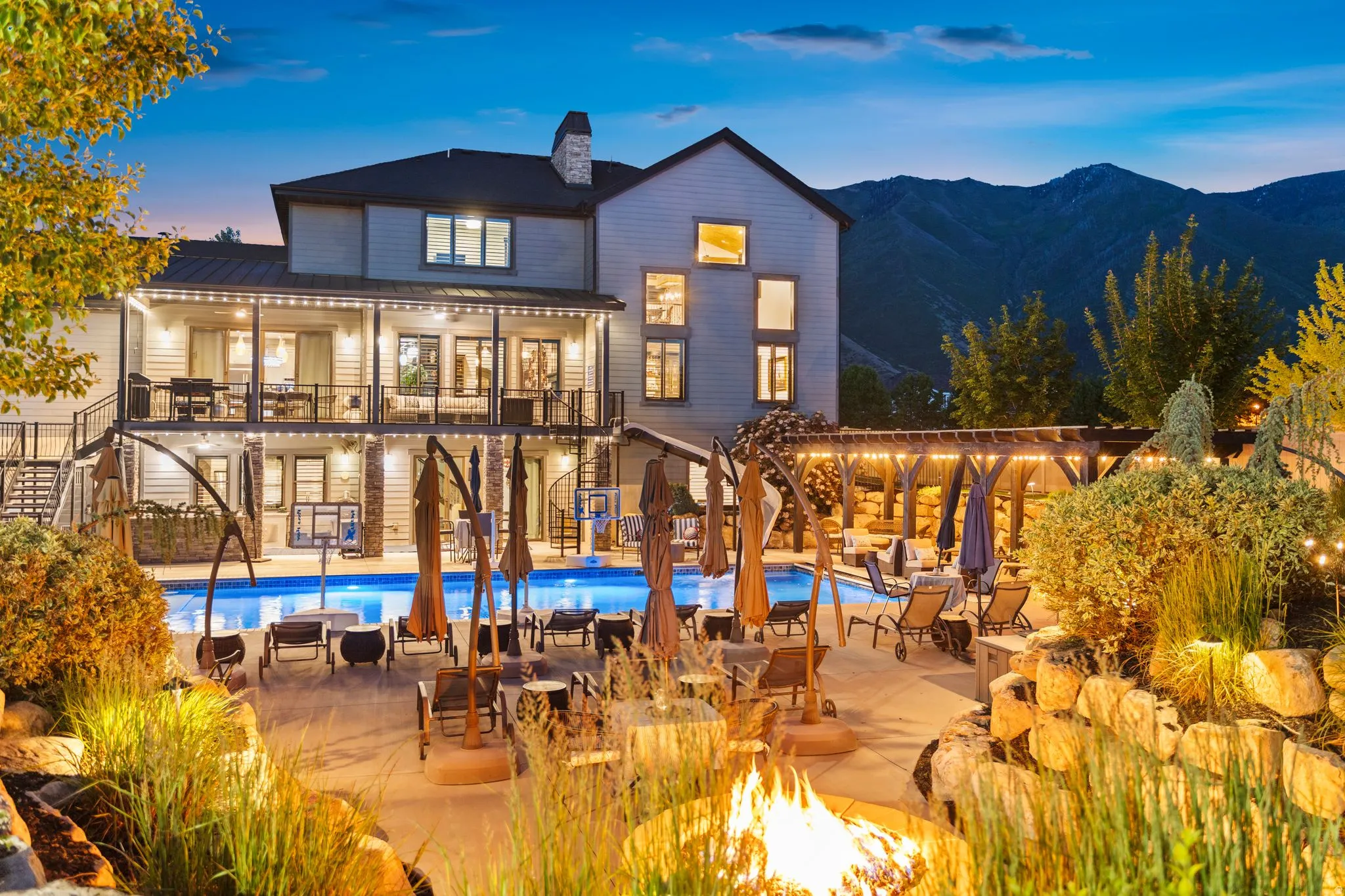 Rear exterior with a large swimming pool, expansive patio, stone fire pit, and a timber pergola