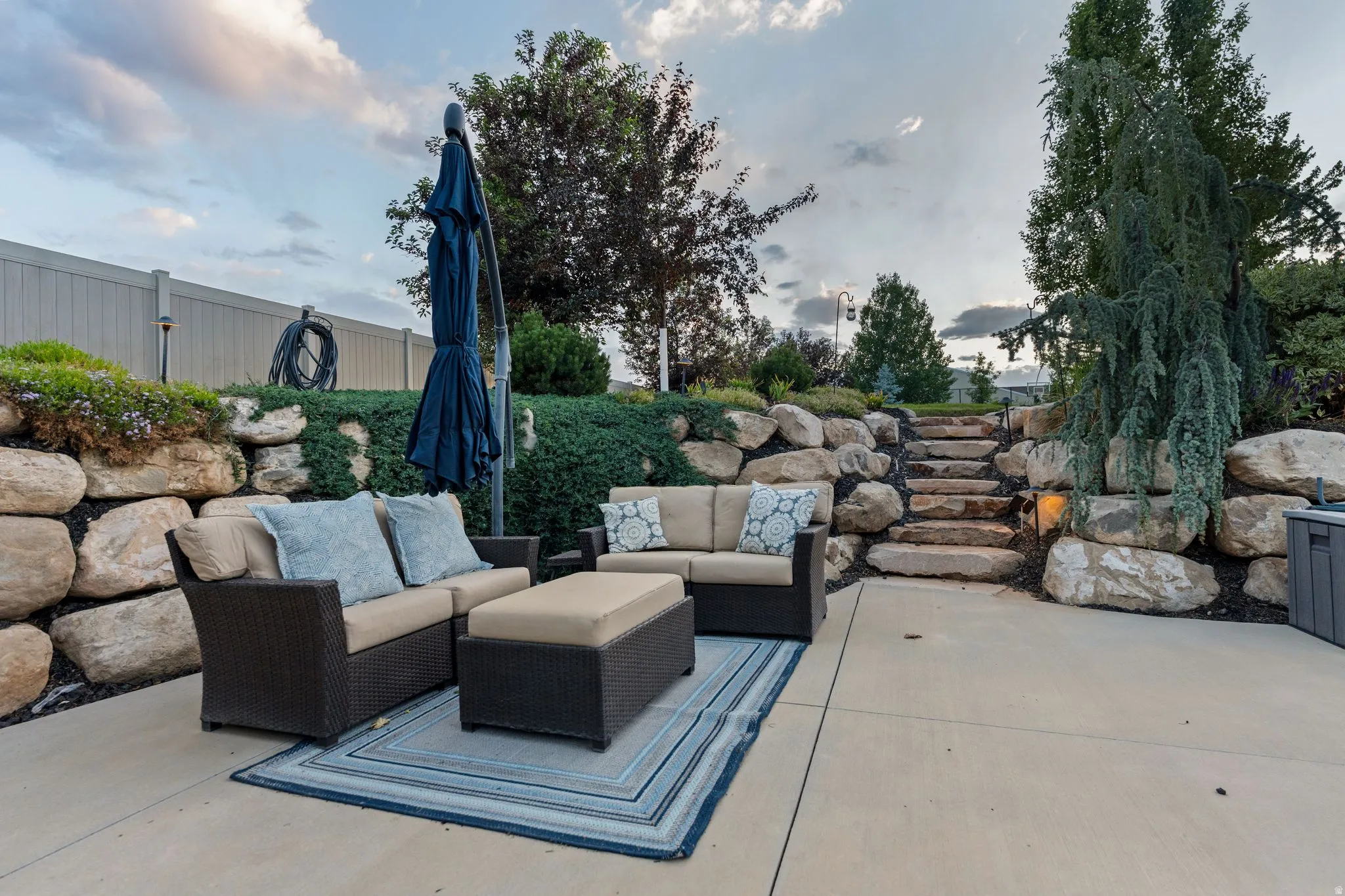 Concrete patio area featuring a natural stone retaining wall and integrated stone steps
