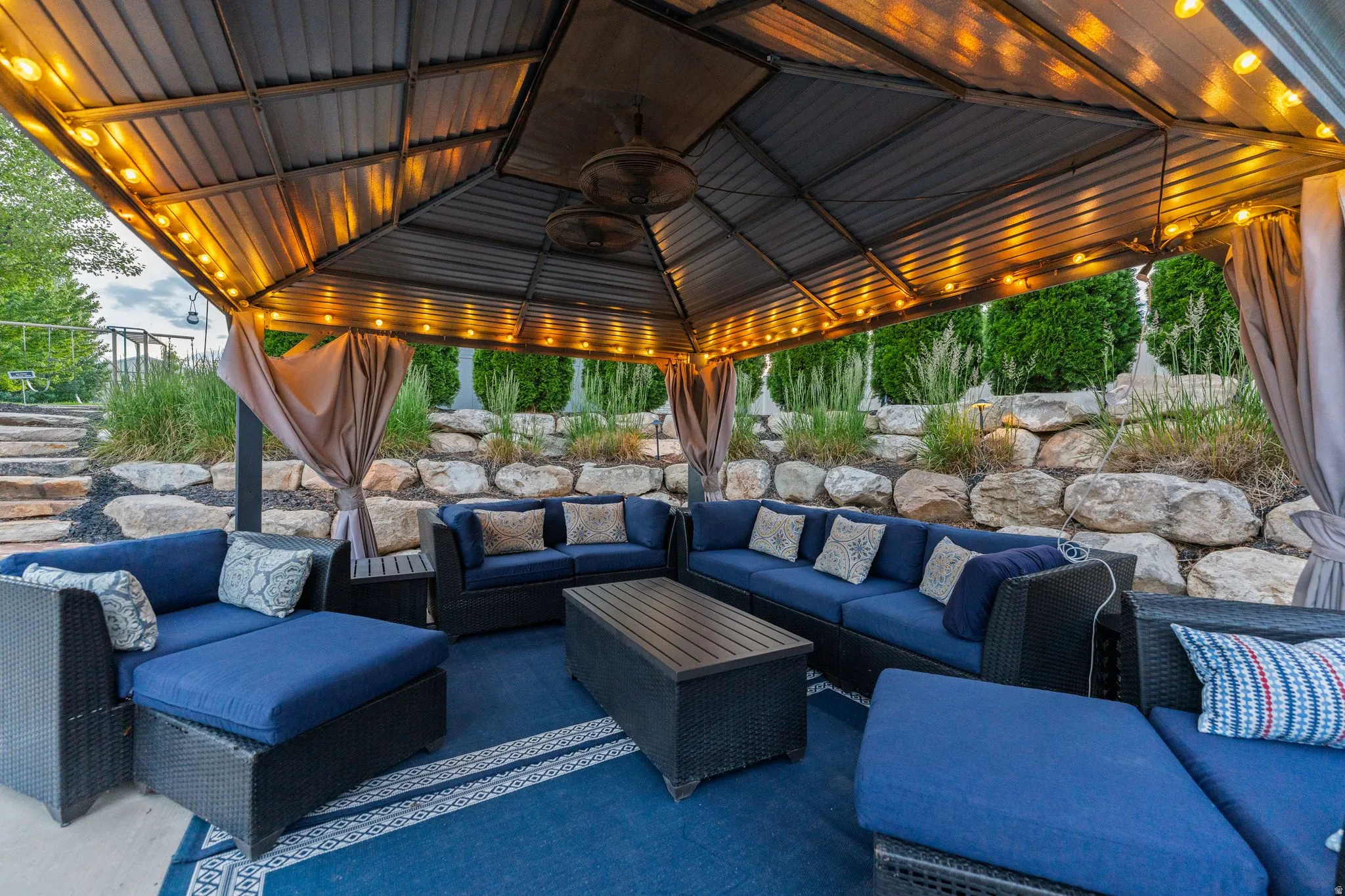 Outdoor gazebo featuring a metal roof, integrated string lights, and privacy drapes
