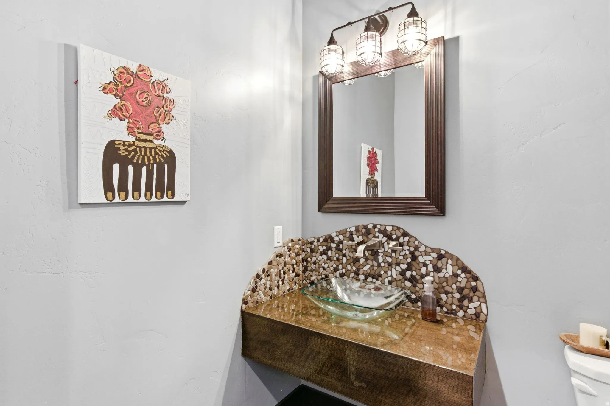 Powder room featuring a wood-finish floating vanity with a vessel sink, a stone mosaic backsplash, and a framed mirror under a three-light fixture