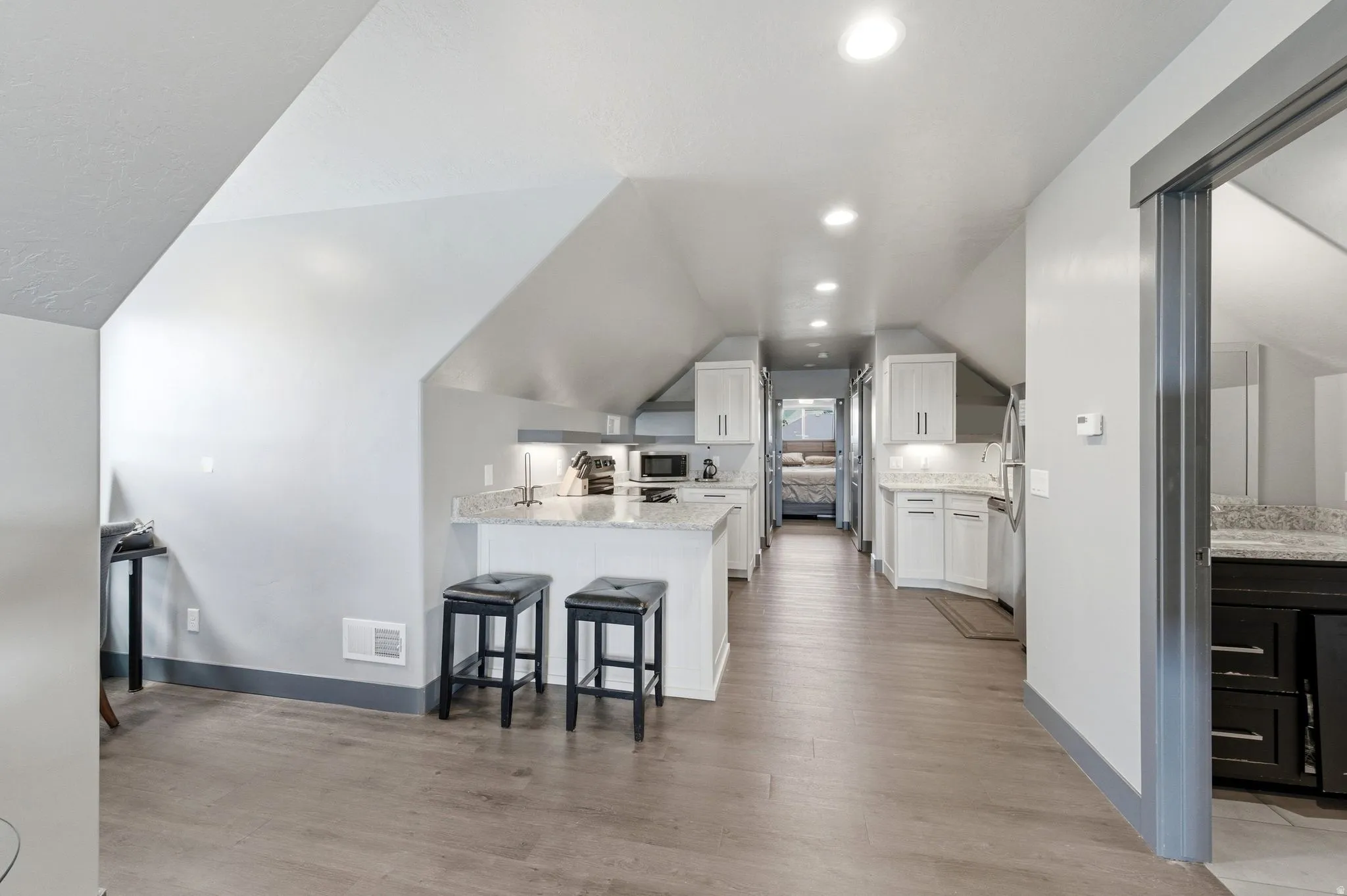 Open-concept living space featuring wood-finish flooring, recessed lighting, and a kitchen with white cabinetry